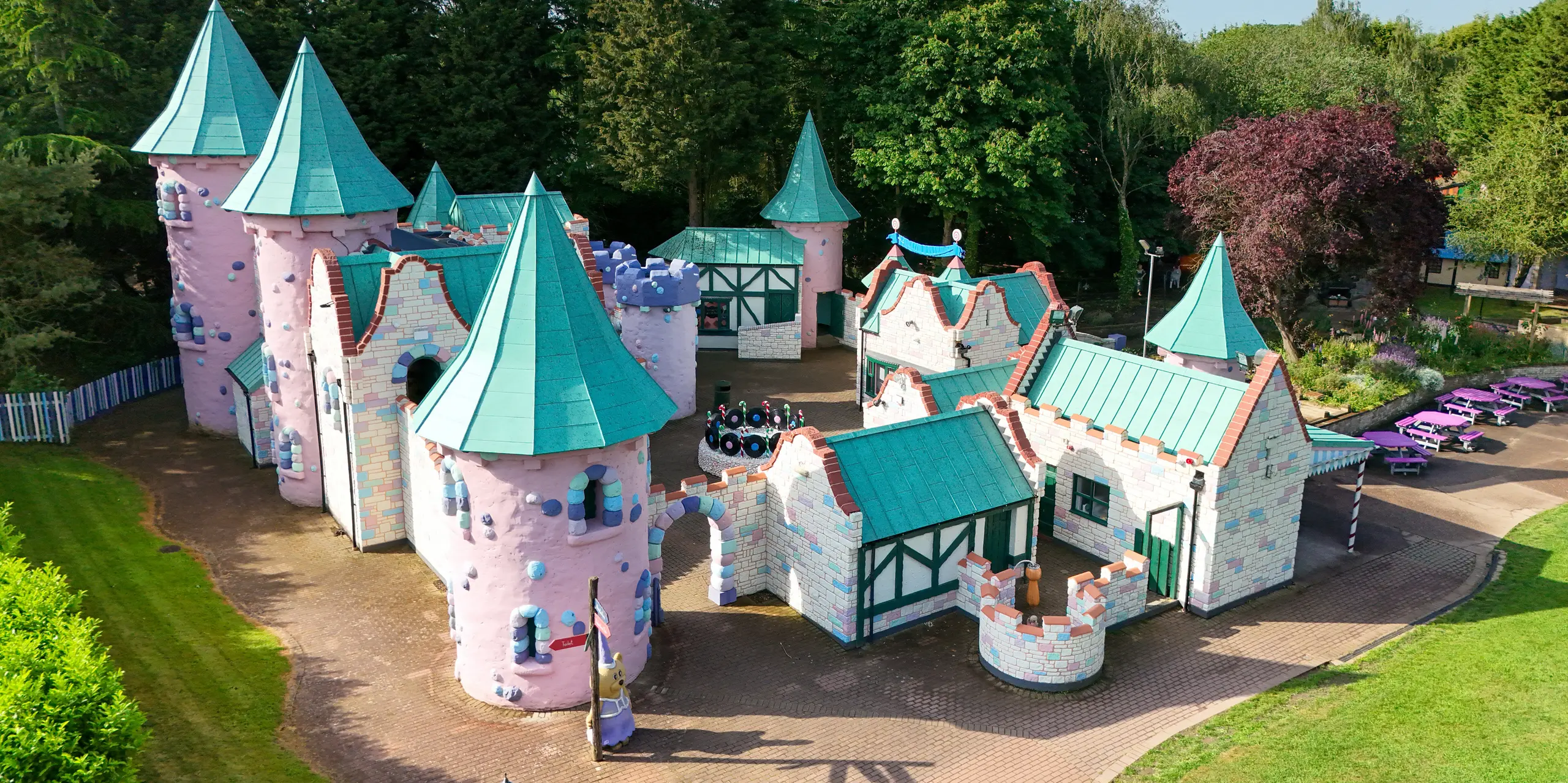 Frontale Ansicht der märchenhaften Schlosskulisse im Sundown Adventureland mit zahlreichen verspielten Türmen, spitzen Kegeldächern und detailreichen Fassaden in Pastellfarben. Die markanten PREFALZ Aluminiumdächer in P.10 Patinagrün fungieren als zentrale Eyecatcher und betonen die fantasievollen Formen mit präzisen Stehfalzen. Unterschiedliche Dachneigungen und komplexe Geometrien werden elegant umgesetzt. Gleichzeitig überzeugen die PREFA Dächer durch hohe Langlebigkeit, Korrosionsbeständigkeit und zuverlässigen Schutz – ideal für dauerhaft beeindruckende Freizeitarchitektur.