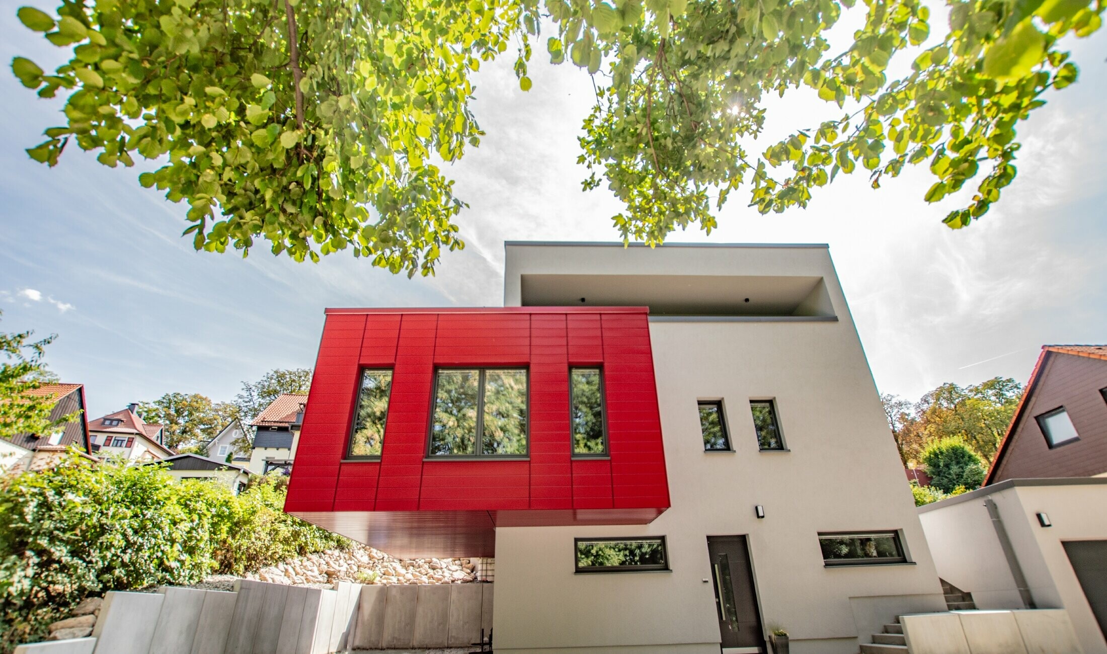 Overhanging building section clad in the PREFA sidings in ruby red. Large red bay window that stands out against the white façade.