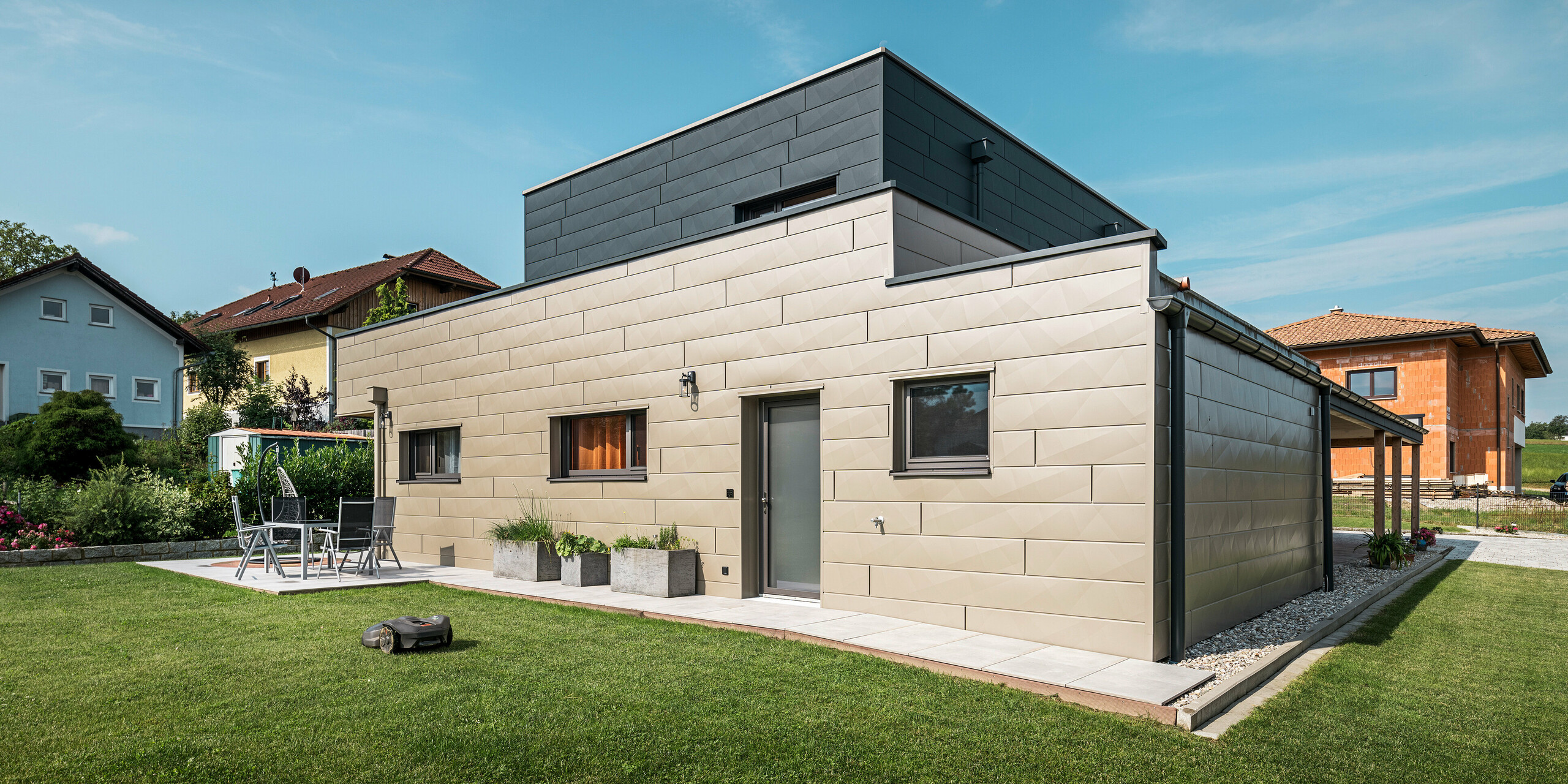 Modernes Einfamilienhaus in Wippenham, Österreich, mit zweifarbiger PREFA Aluminiumfassade in Bronze und Anthrazit. Die Fassade ist mit Siding.X Fassadenpaneelen gestaltet, die für eine elegante und zeitgemäße Optik sorgen. Die integrierte PREFA Dachentwässerung mit Wasserfangkasten und Ablaufrohr sowie eine gepflegte Gartenanlage mit Terrasse betonen das moderne Design des Hauses.