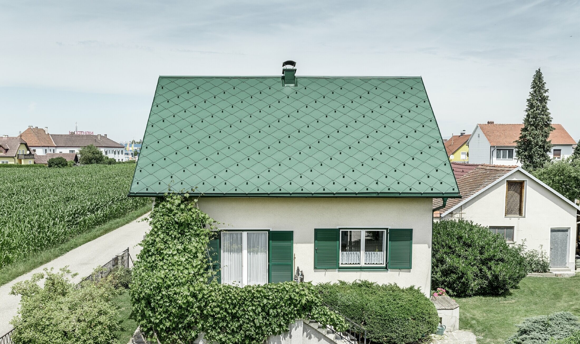 Classic detached house with a gable roof with an aluminium roof covering in moss green with green shutters. The roof was covered with PREFA rhomboid roof tiles 44 × 44 in P.10 moss green.