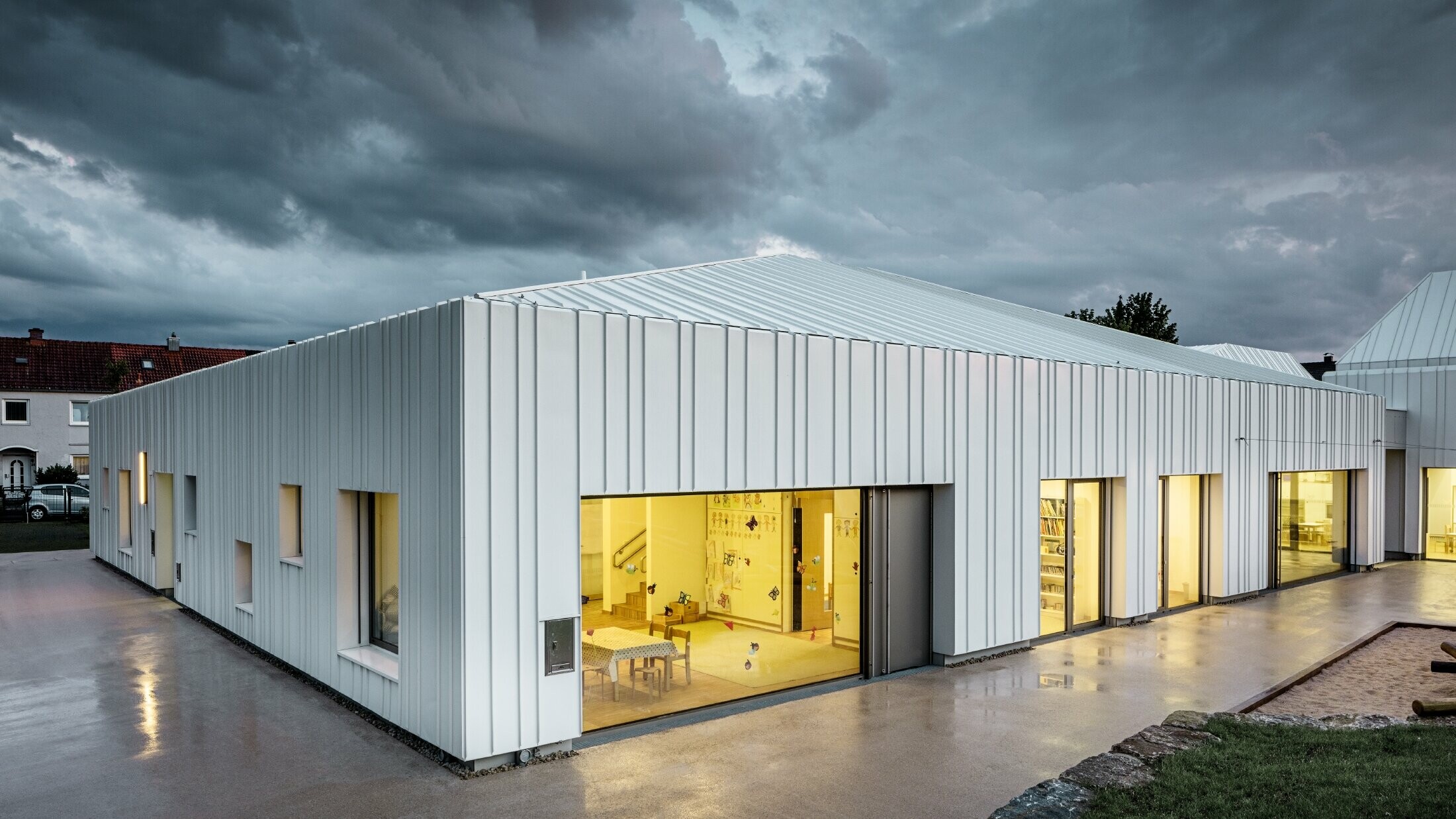 Day nursery in Niederwerrn with PREFALZ roof and façade in pure white with different widths of panels photographed at dusk and in a cloudy atmosphere