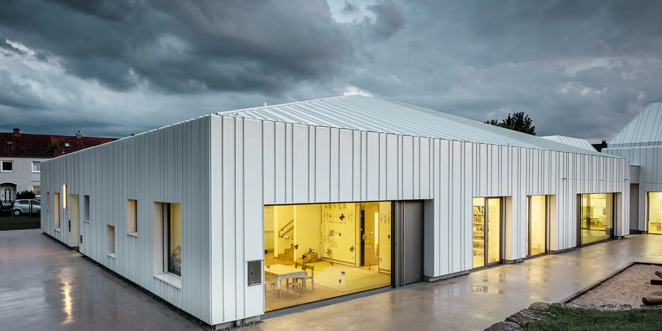 Day nursery in Niederwerrn with PREFALZ standing seam roof and façade in pure white with different widths of panels photographed at dusk and in a cloudy atmosphere