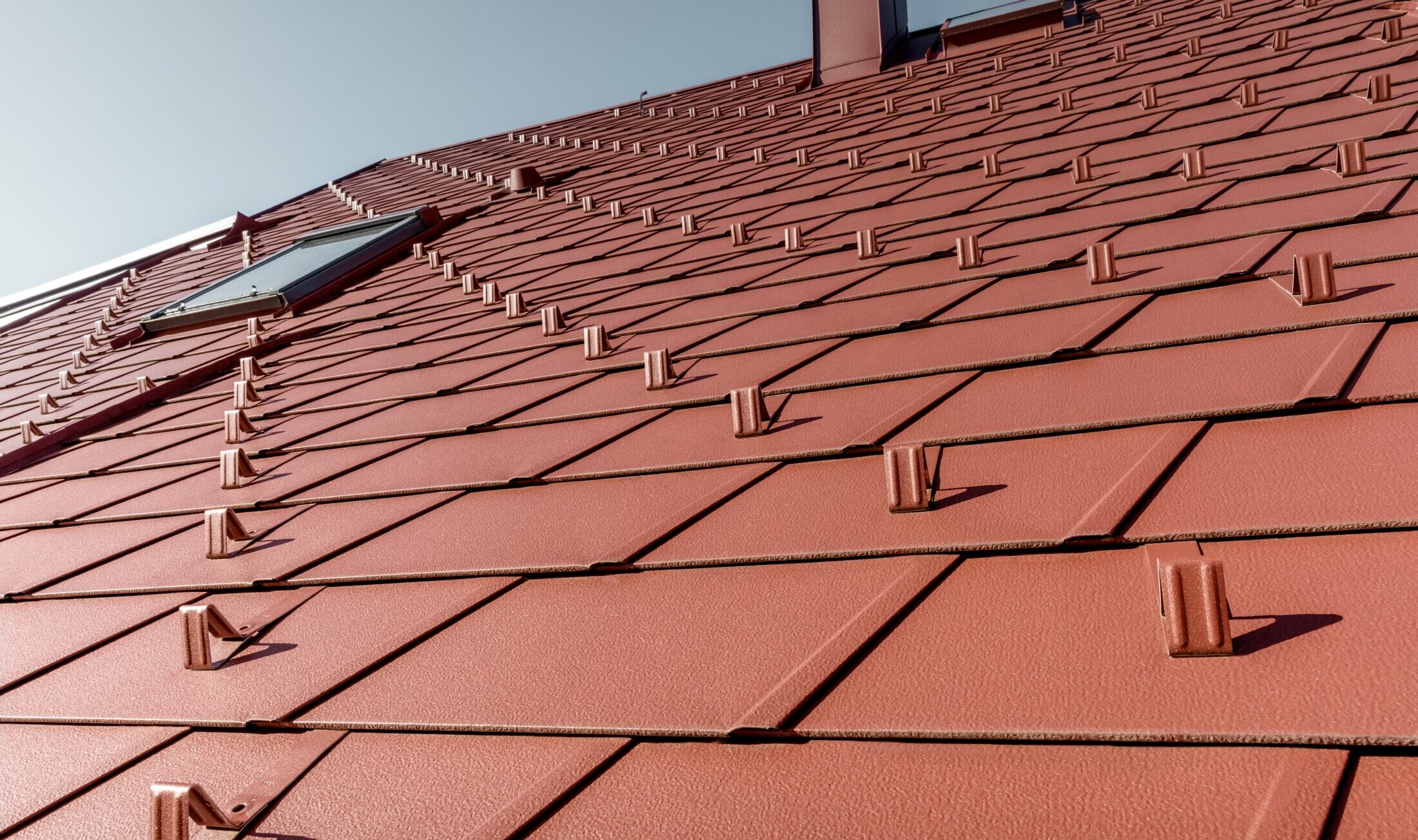 Close-up of the PREFA DS.19 roof shingle in P.10 oxide red with snow guards and roof windows.
