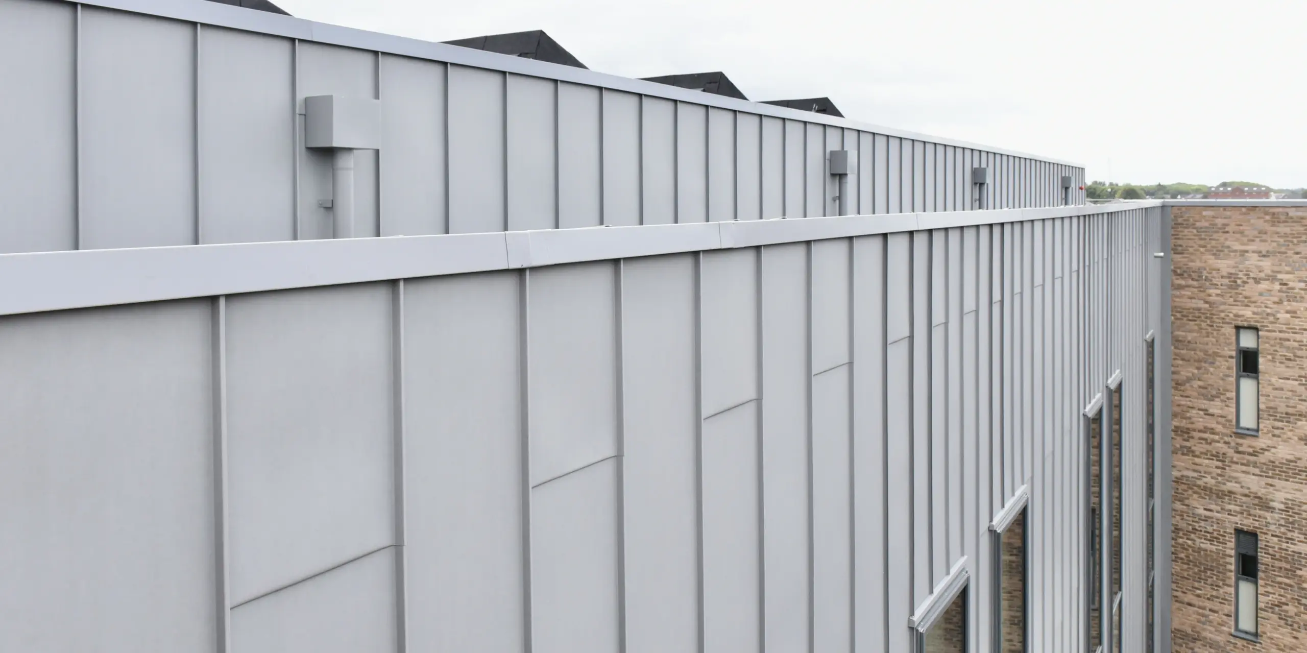 Detailed view of the PREFALZ (standing seam) aluminium facade in patina grey at the Regional College North, UK. The clear lines and matt appearance of the standing seam cladding emphasise the high-quality workmanship and timeless design.