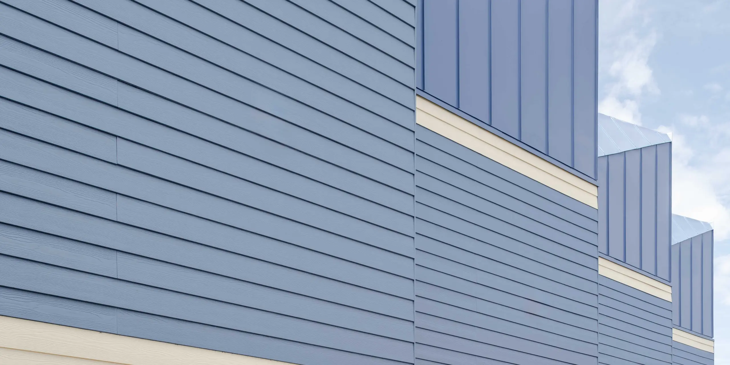 The photograph shows the striking façade of the Goldsmith Mews terraced houses with their eye-catching dusty blue PREFA FALZONAL standing seam aluminium cladding. The precise vertical lines of the aluminium surfaces create a lively structure and emphasise the modern architecture. The light-coloured basements lend the ensemble a sense of lightness and enhance the colour contrast. The durable, colour-stable PREFA aluminium provides long-term protection against the weather and enables a clear, long-lasting design that gives the project its distinctive character.