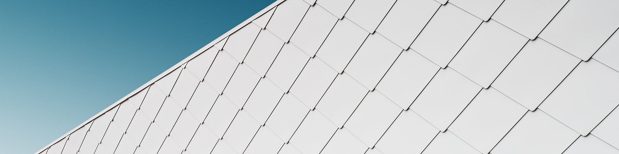 Detailed view of the façade with the evenly laid façade tiles, the sky extending above it.