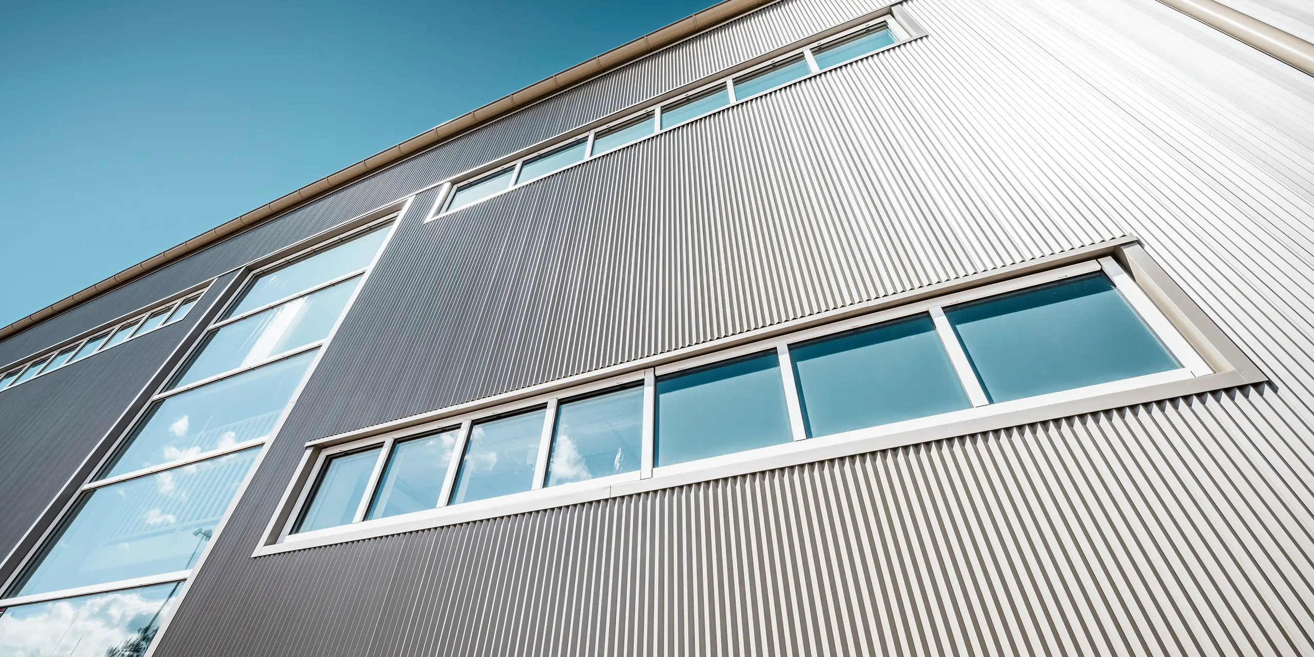 Exterior view of the Park Arena in Värnamo, Sweden, with a modern PREFA façade in bronze. The serrated aluminium profiles create striking light and shadow effects. The recessed windows blend harmoniously into the precisely crafted façade, which stands for durability, resilience and contemporary design.