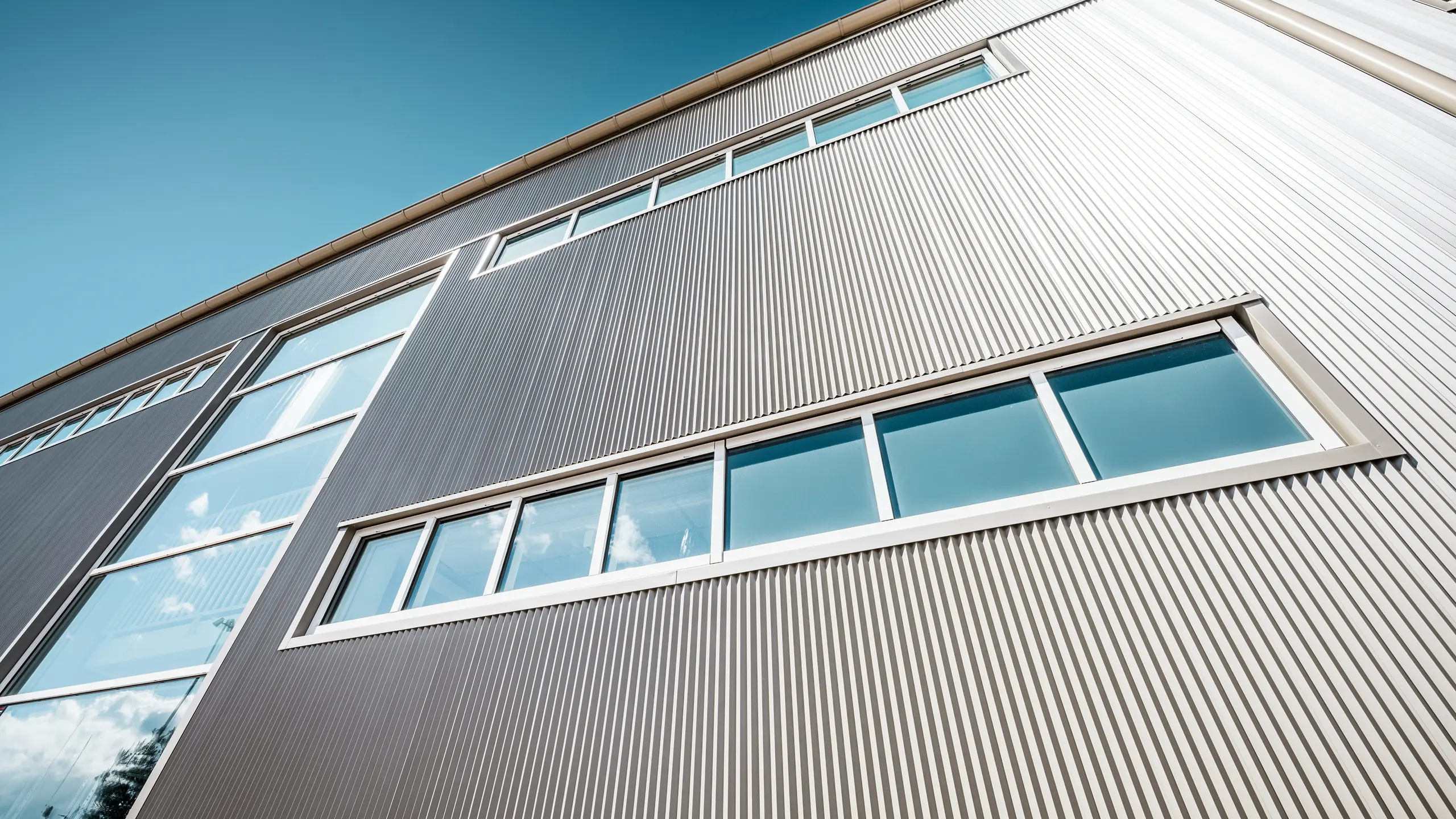 Exterior view of the Park Arena in Värnamo, Sweden, with a modern PREFA façade in bronze. The serrated aluminium profiles create striking light and shadow effects. The recessed windows blend harmoniously into the precisely crafted façade, which stands for durability, resilience and contemporary design.
