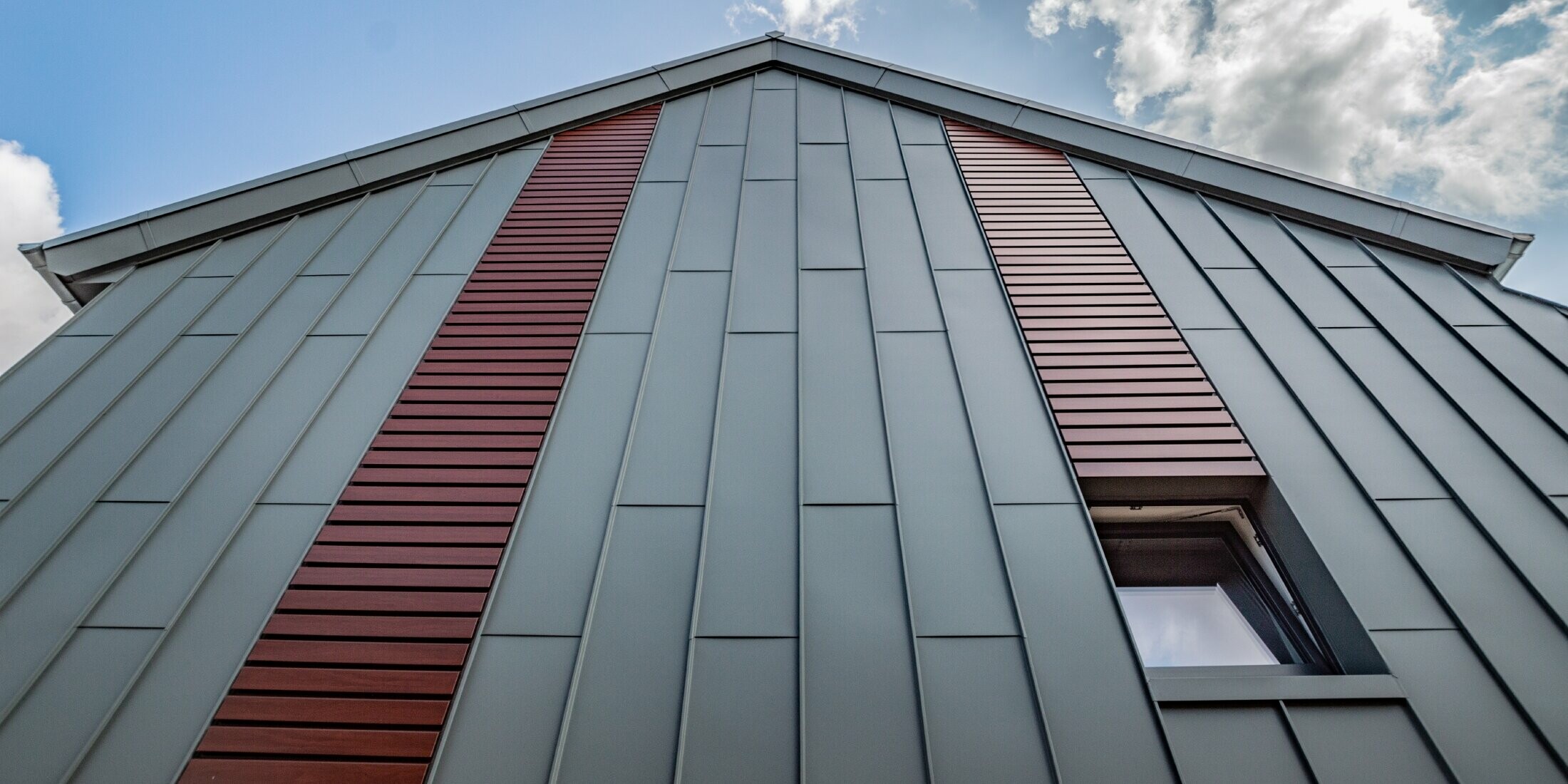 Vertical angled standing seam façade with panel covering in light grey, as well as siding horizontally in dark wood by PREFA.