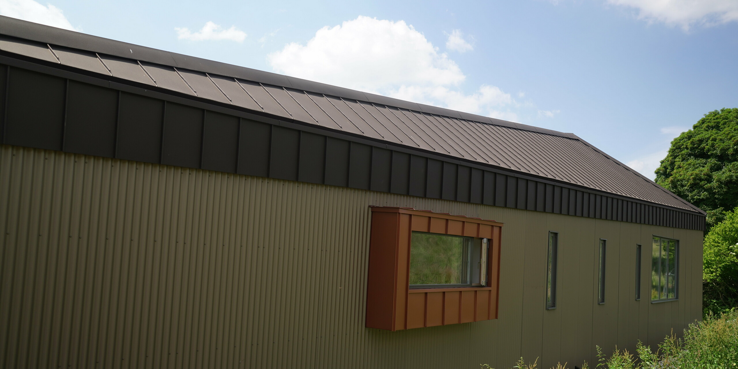 Longhouse with aluminium roof made of PREFALZ in P.10 Brown and window cladding made of Falzonal in the colour New Copper