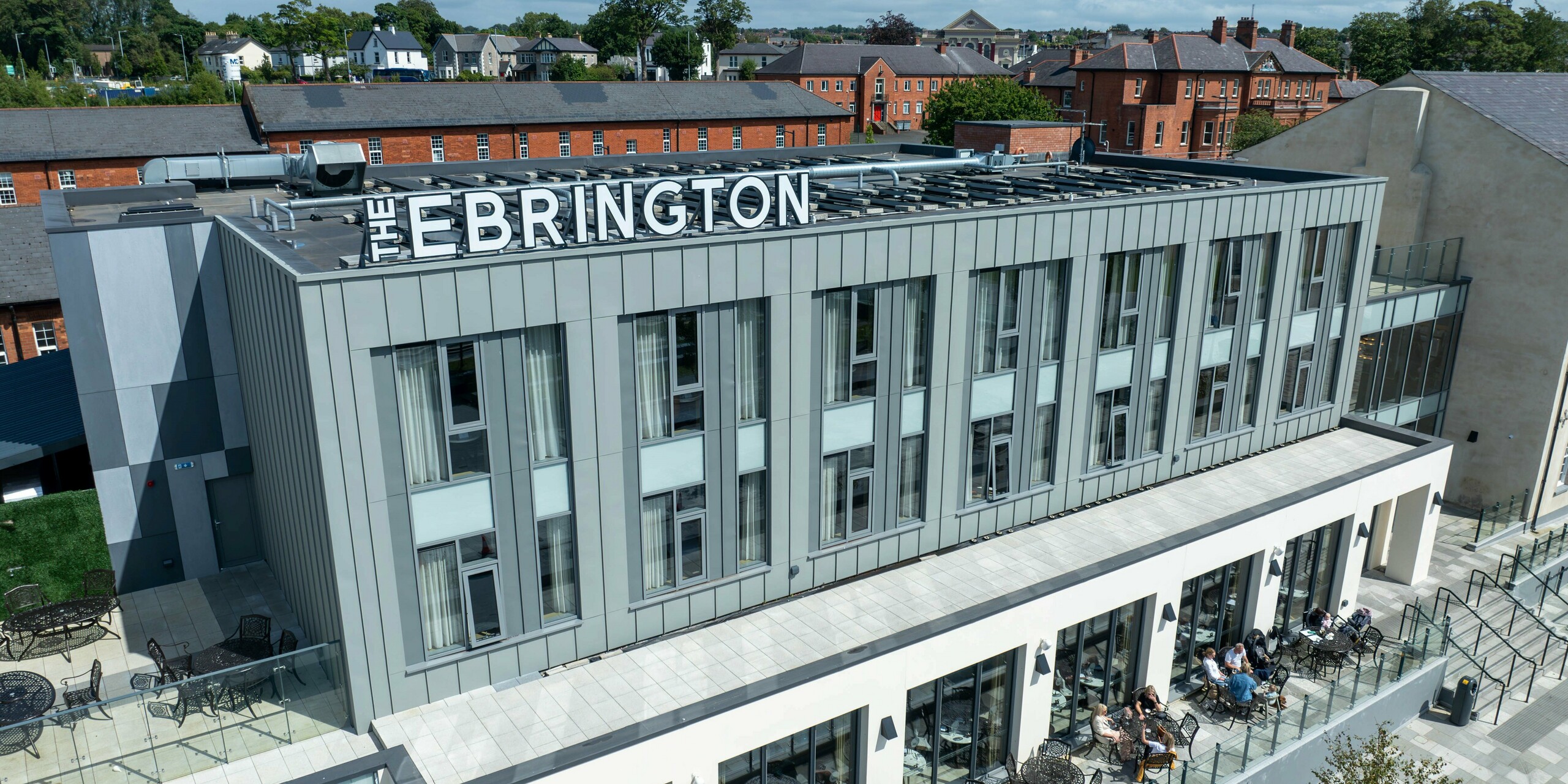 The Ebrington Hotel in the centre of Londonderry, Northern Ireland, impresses with its modern PREFALZ aluminium cladding in the colours P.10 Light Grey and P.10 Zinc Grey. This high-quality, hard-wearing sheet metal façade gives the building an elegant and robust appearance. The building envelope emphasises the contemporary architecture of the hotel, while the terrace in the foreground provides an inviting space for guests. Historic buildings can be seen in the background, providing an interesting contrast to the modern design of the Ebrington Hotel.