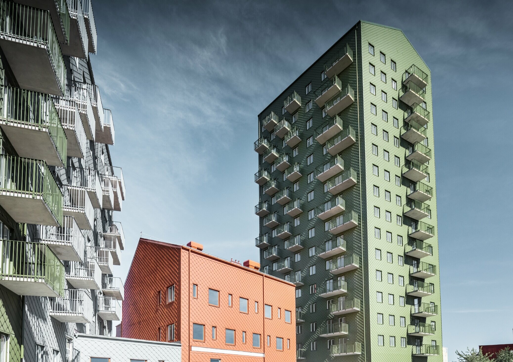 Multiple residential buildings clad in the PREFA 29 x 29 rhomboid façade tile in the colours olive green, brick red and light grey in Gothenburg, Sweden.