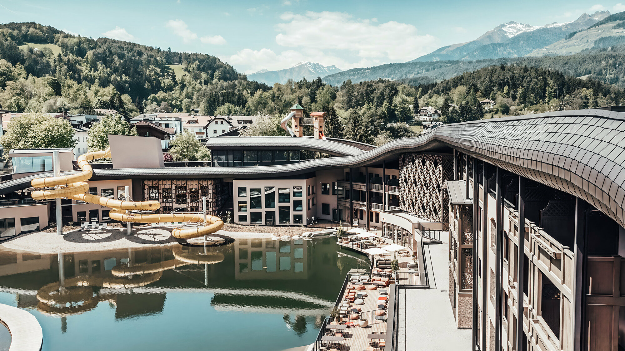 Overview of the hotel with lake and water slide. In the background hilly and wooded area can be seen.