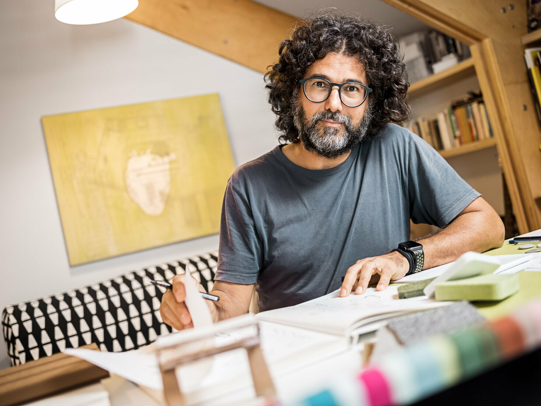 Portrait of architect Sebastiano Longaretti in his atelier at his home, one of his paintings is hanging on the wall behind him and he is leafing through a sketch pad.