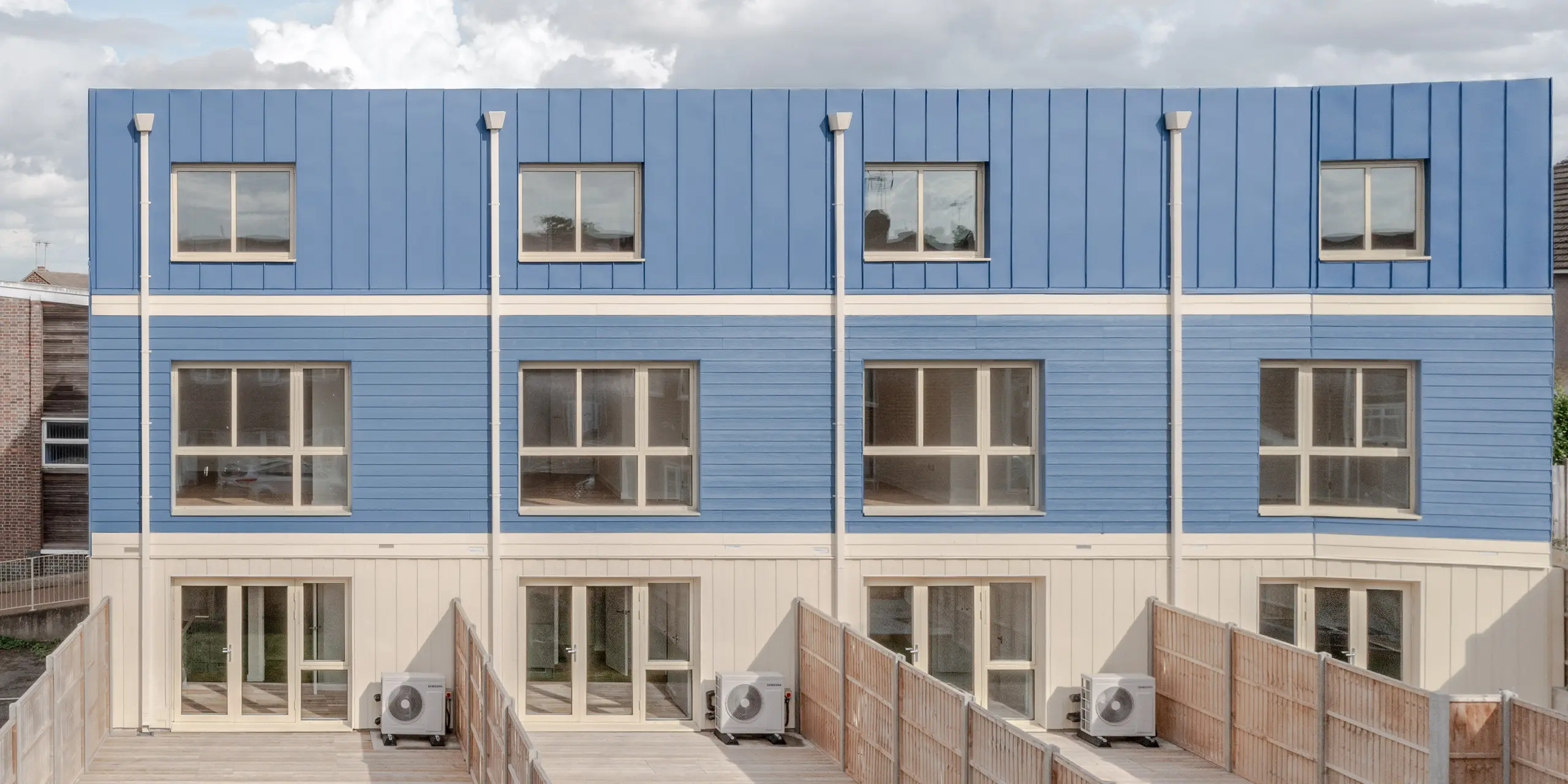 The garden side of the terraced houses in Goldsmith Mews features the striking dusty blue FALZONAL standing seam façade and roof design, which gives the buildings a clear, modern character. The precise vertical folds and blue panels create a rhythmic, lively façade. The bright ground floor areas and large windows open up the architecture to the external environment. The high-quality PREFA aluminium offers lasting weather protection, high colour and shape stability, and enables a durable, aesthetic design with high recognition value.