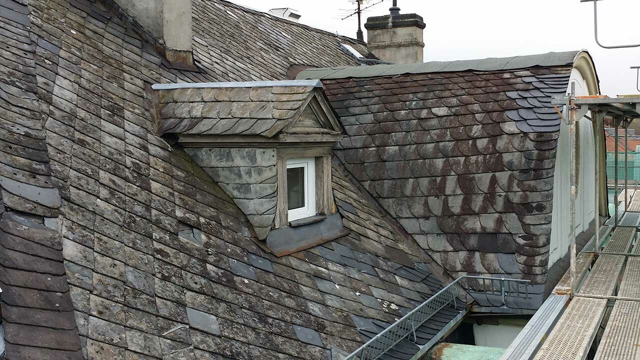 Hotel in Bad Kissingen before renovation with PREFA rhomboid roof tiles; the roofing elements are covered in moss and in dire need of renovation.