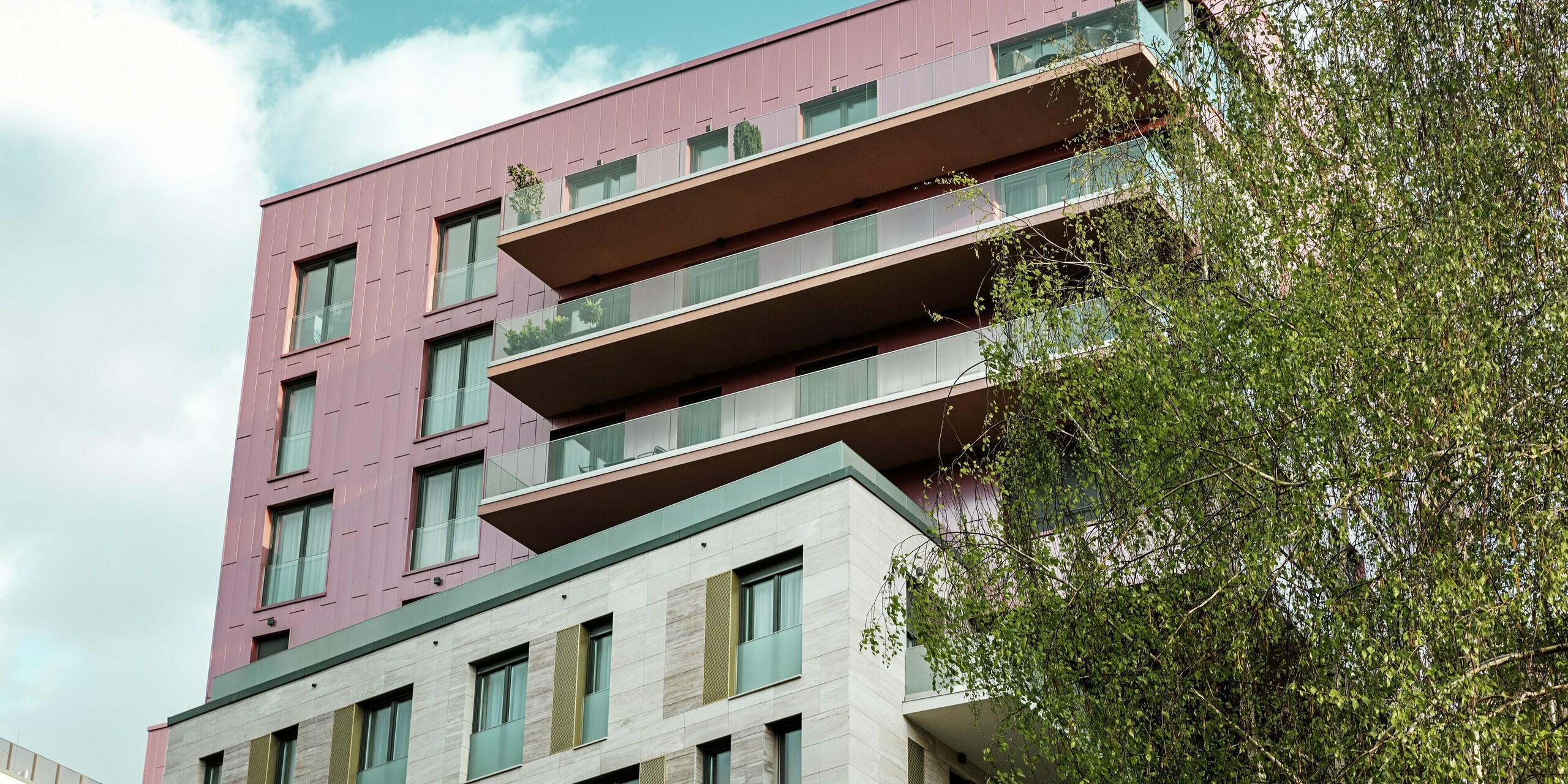 Oberer Gebäudeteil des Wohnkomplexes „Grand Corvin“ in Budapest mit markanter PREFA Siding Aluminiumfassade in vertikaler Verlegung und Sonderfarbe Lachsmetallic, gebürstet. Die hochwertigen Fassadenpaneele verleihen dem Gebäude ein modernes, elegantes Erscheinungsbild und setzen einen auffälligen architektonischen Akzent im revitalisierten Corvin-Viertel.