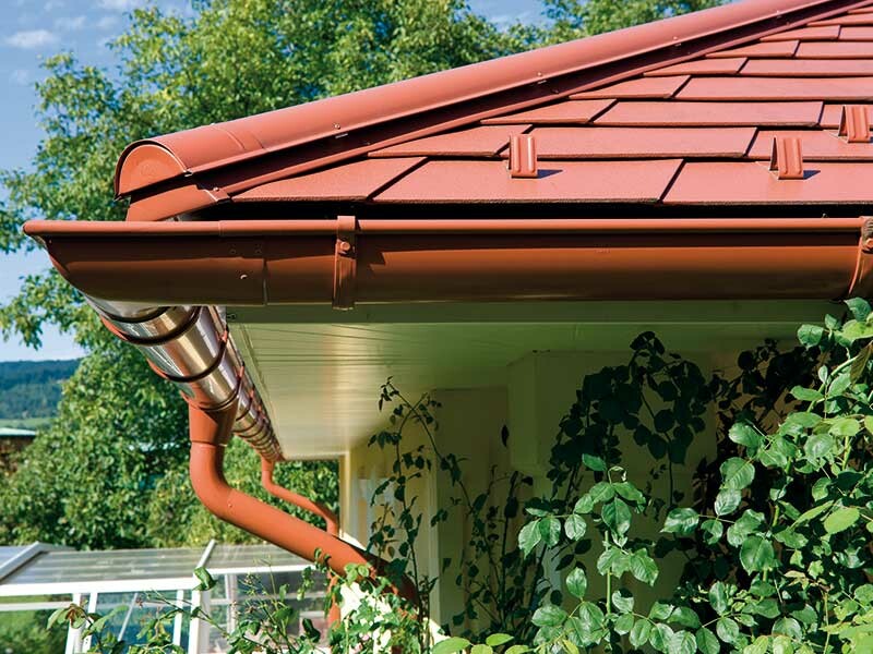 Detailed image of PREFA shingles in brick red with matching guttering, also in brick red.