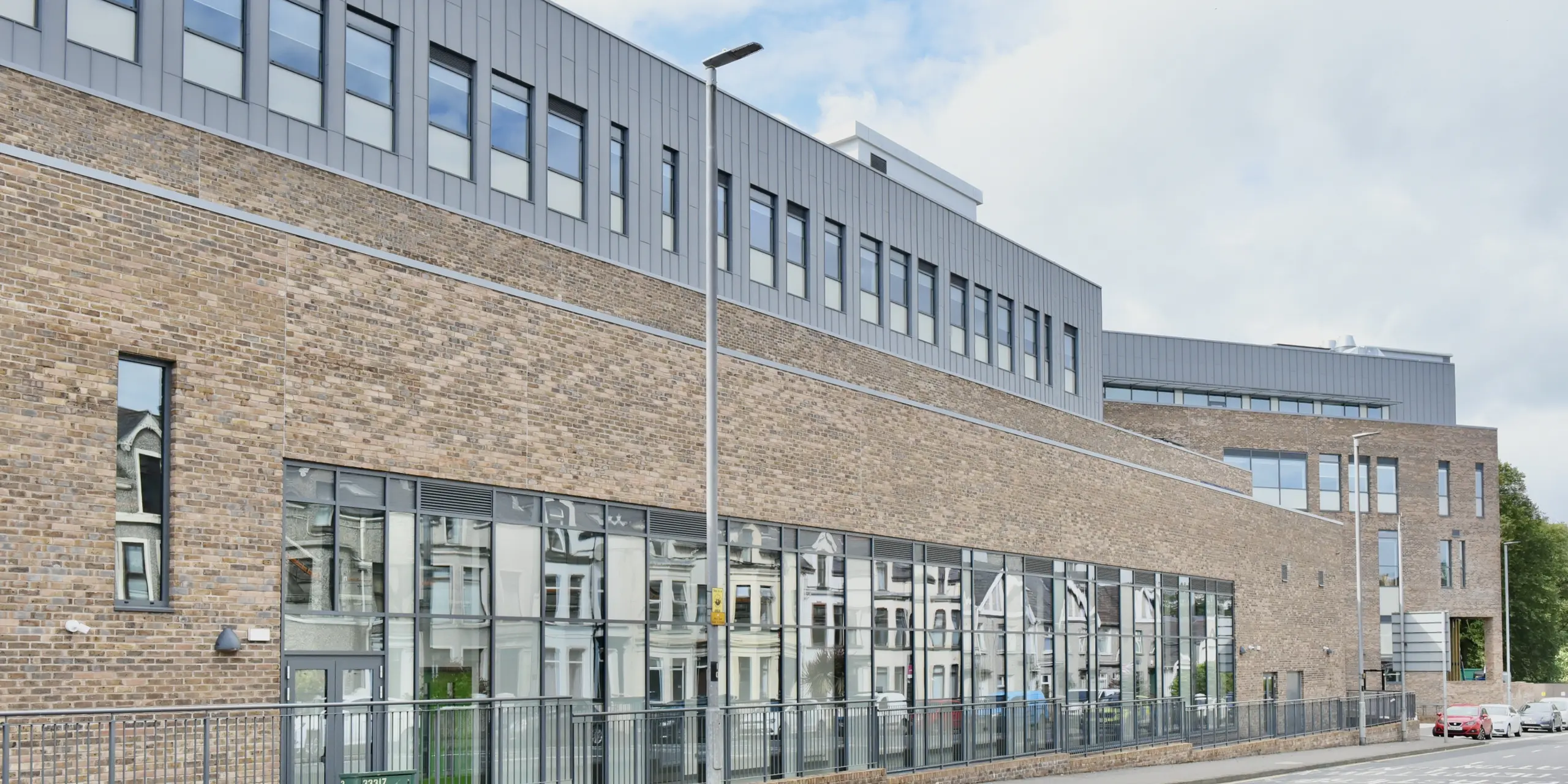 Street view of the North Regional College in Coleraine, Northern Ireland. The precisely crafted PREFALZ standing seam aluminium facade in patina grey complements the traditional architecture and harmonises with the classic brick look. Functionality and design combine to create an impressive building.