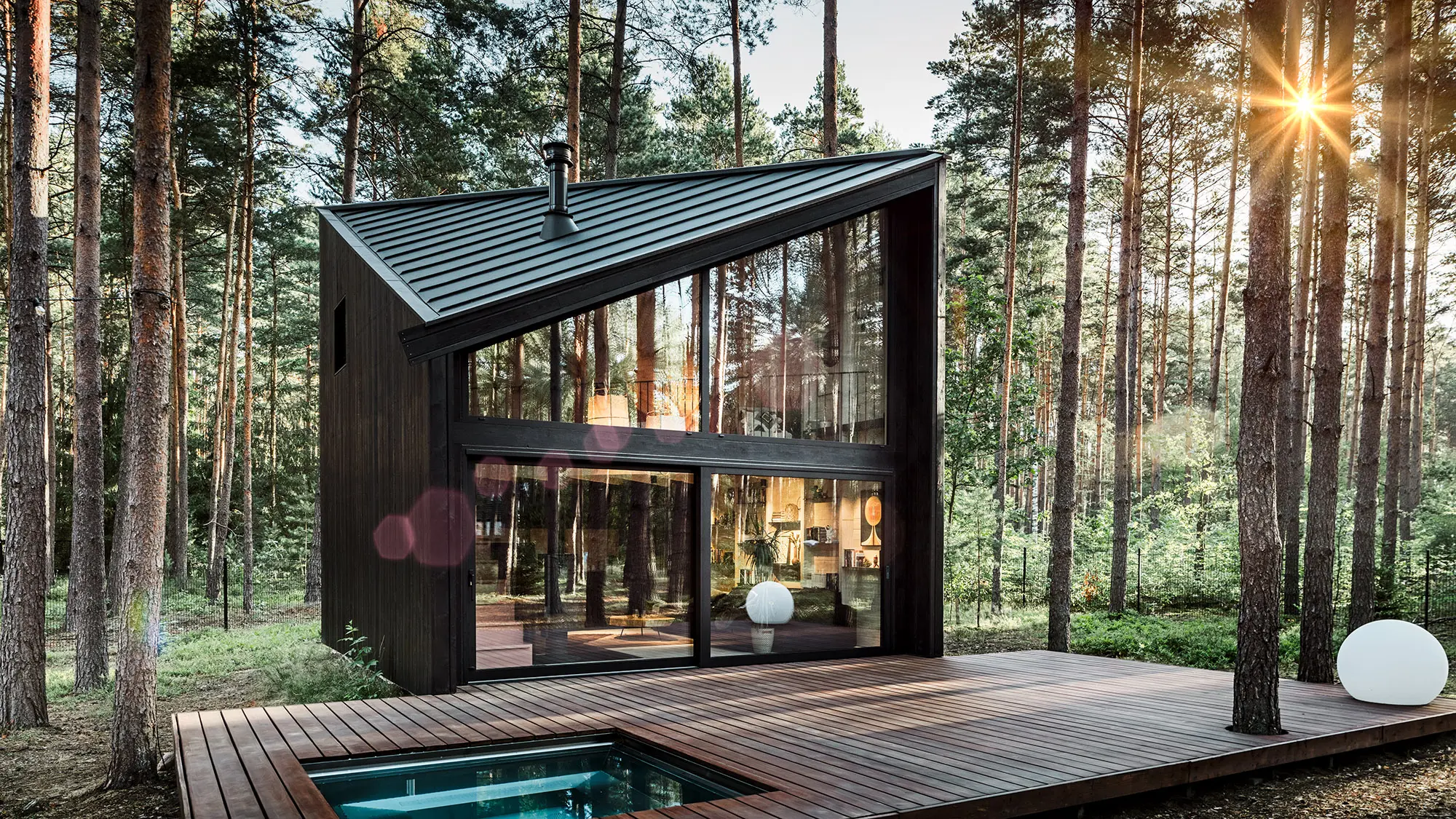 Side view of the holiday home with its diagonal Prefalz roof. The natural surroundings are reflected in the glazing.