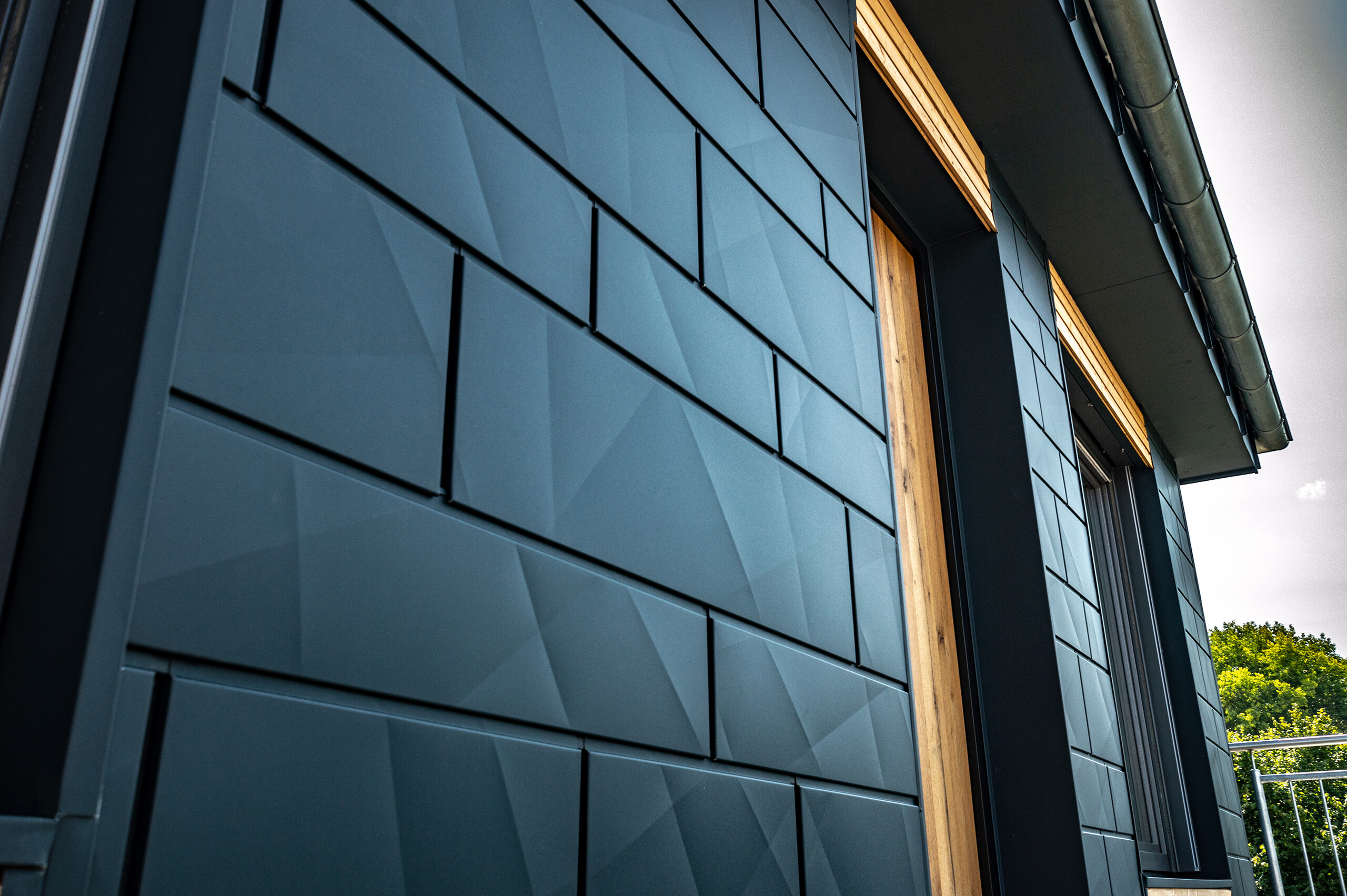 Façade with PREFA Siding.X in anthracite with balcony doors and large glazed areas mixed with a wooden façade.