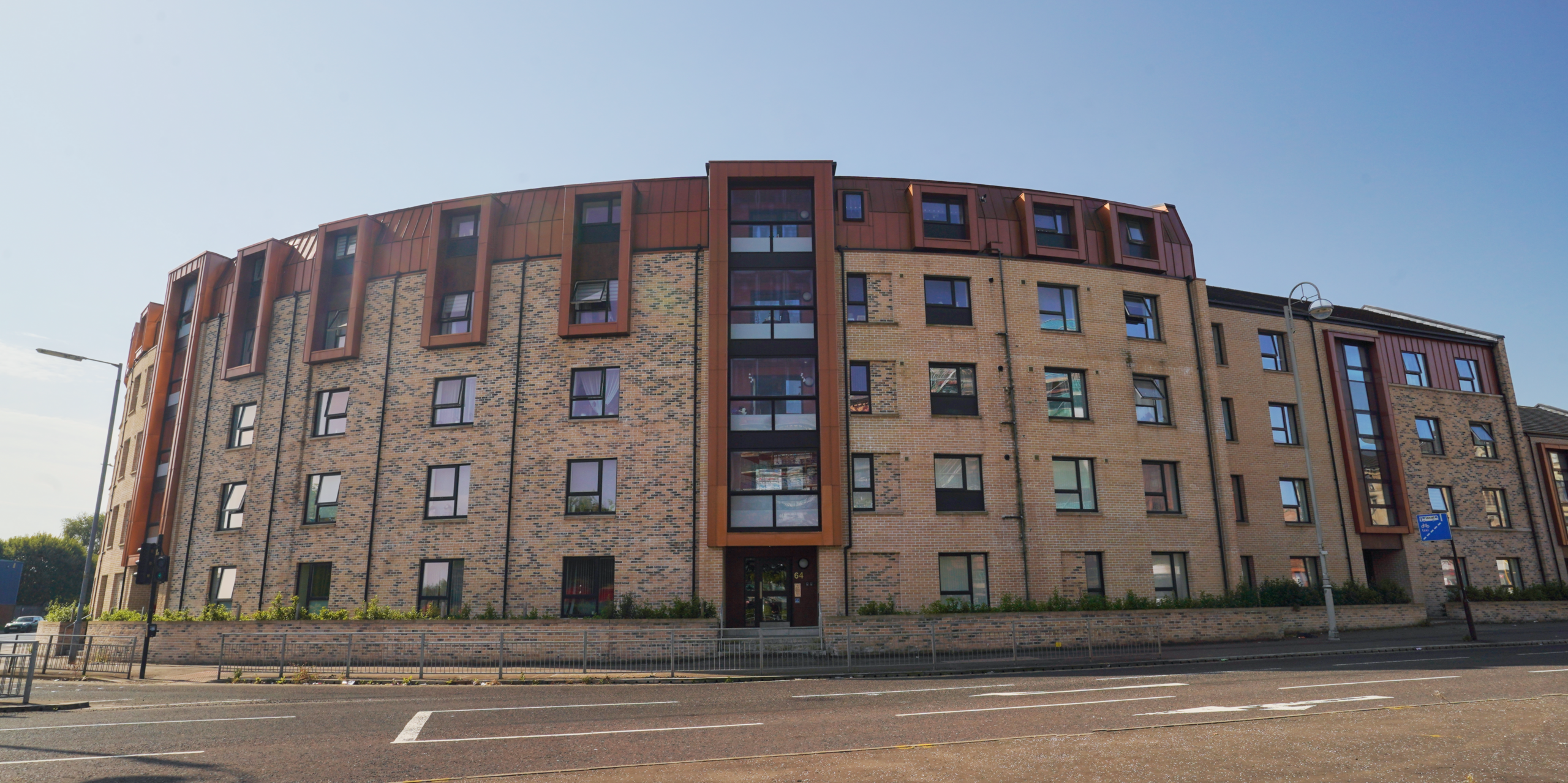 View from the street of a modern residential complex on Nethan Street in Glasgow. The residential development stands out thanks to the use of around 500m² of FALZONAL in the colour New Copper on the roof and façade sections. The warm copper colour of the aluminium complements the brick structure of the building and gives the property a contemporary and sophisticated look. The harmonious integration of colour and material underlines the desire to design urban living space in an aesthetic and functional way.