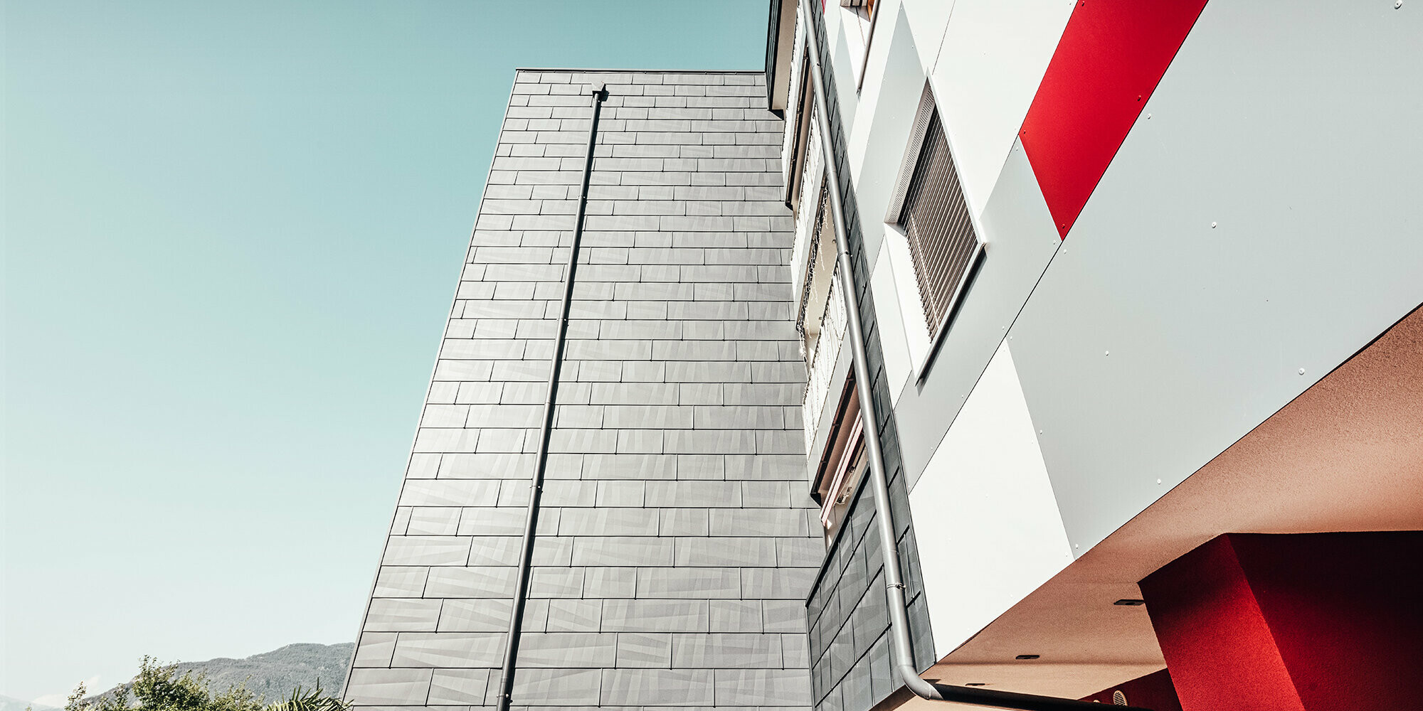 Close-up from below. In the front: the anthracite-coloured PREFA façade. Right: the white, grey and red façade front.