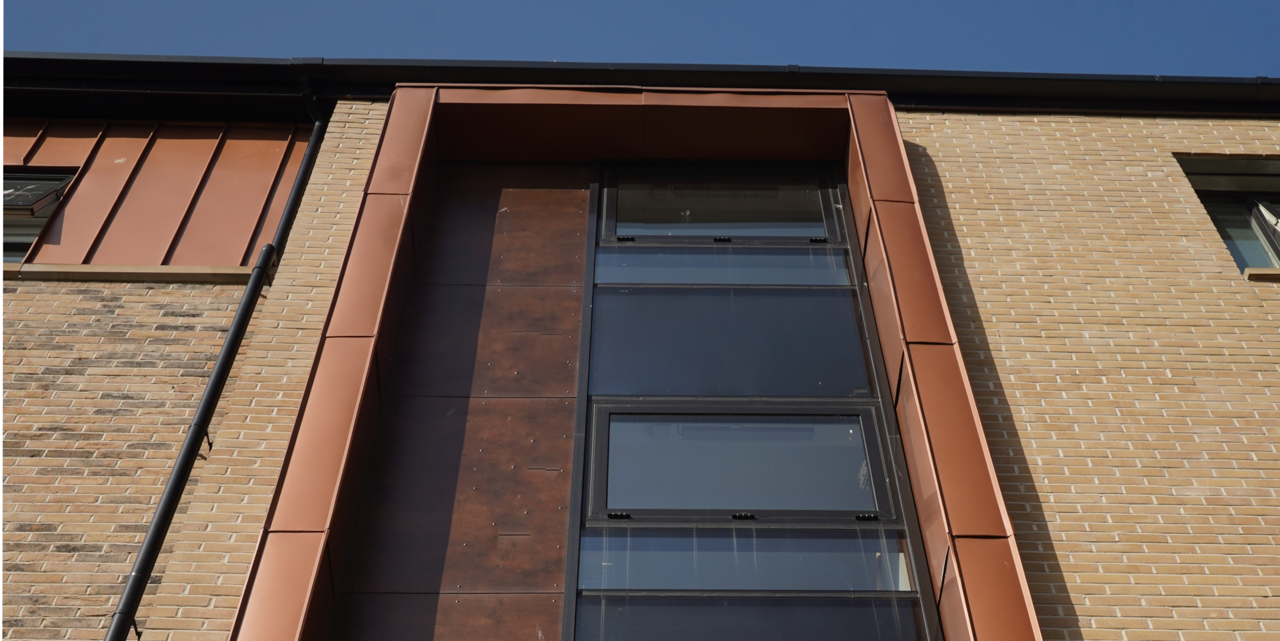 Close-up of a window area on the façade of a residential development on Nethan Street in Glasgow, framed by FALZONAL in New Copper. This high quality PREFA aluminium product complements the clean glass architecture with its warm copper colour, creating a visual link between modern construction and traditional materials. The FALZONAL finish emphasises the precise and sophisticated design of the residential building.