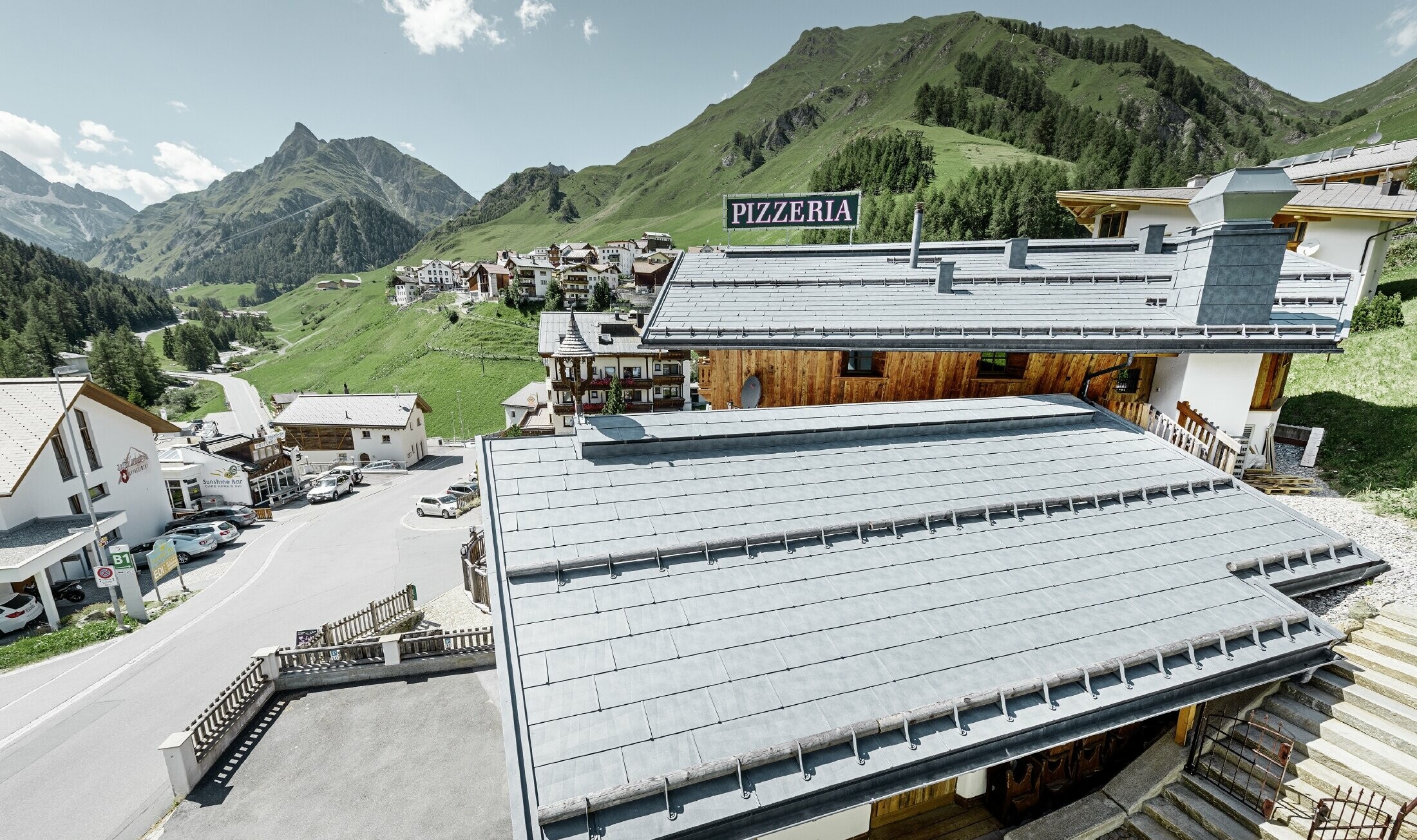 Restaurant Almrausch with a mountainous backdrop and a PREFA roof with FX.12 roof panels in stone grey and mountain snow guard brackets