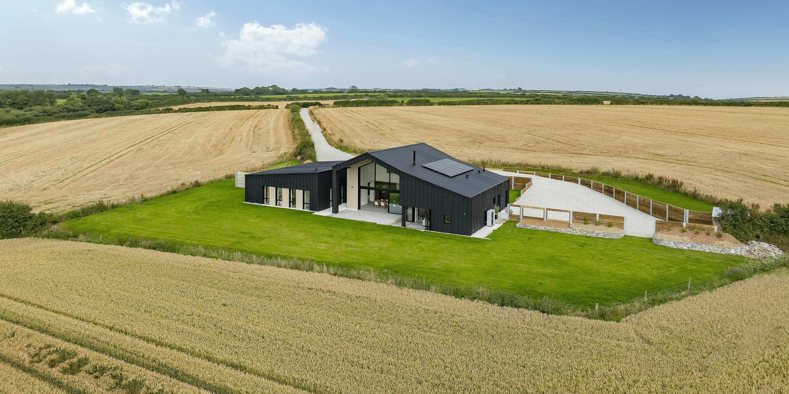 Panoramic view from ‘The Hide’ in Cornwall, nestled among wide fields. In front of the house, there is a well-kept green area. The modern detached house impresses with an anthracite-coloured PREFALZ aluminium shell in the proven P.10 coating. The roof and façade harmonise perfectly with the natural environment. The clear standing seam look gives the building elegance and durability.