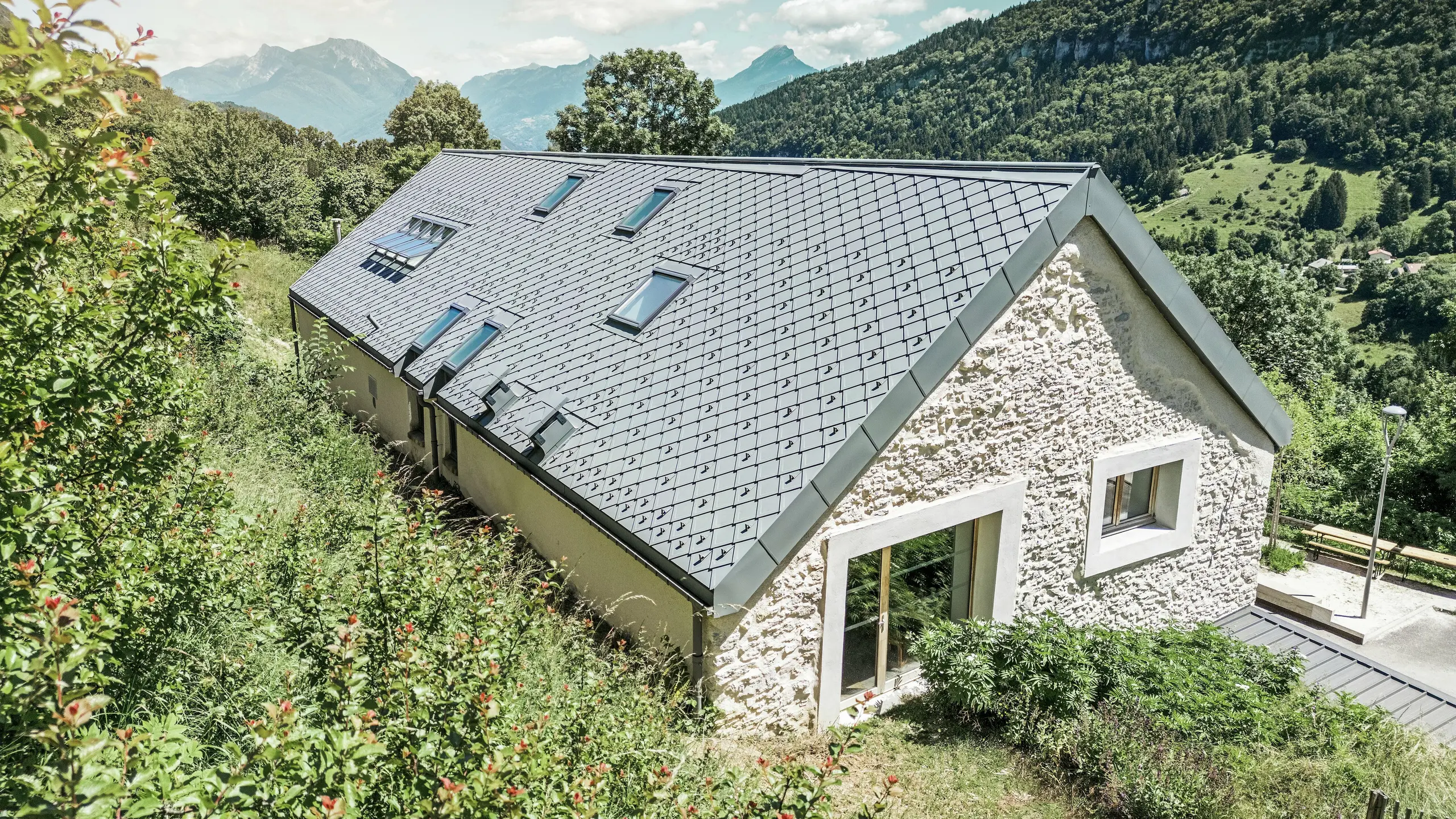 View of the roof of the renovated barn ‘La Grange à Gaby’ in Engins, France. The building is covered with long-lasting PREFA 29 × 29 rhombic tiles, which combine modern protection with traditional aesthetics. The idyllic mountain landscape emphasises the harmonious integration into nature.