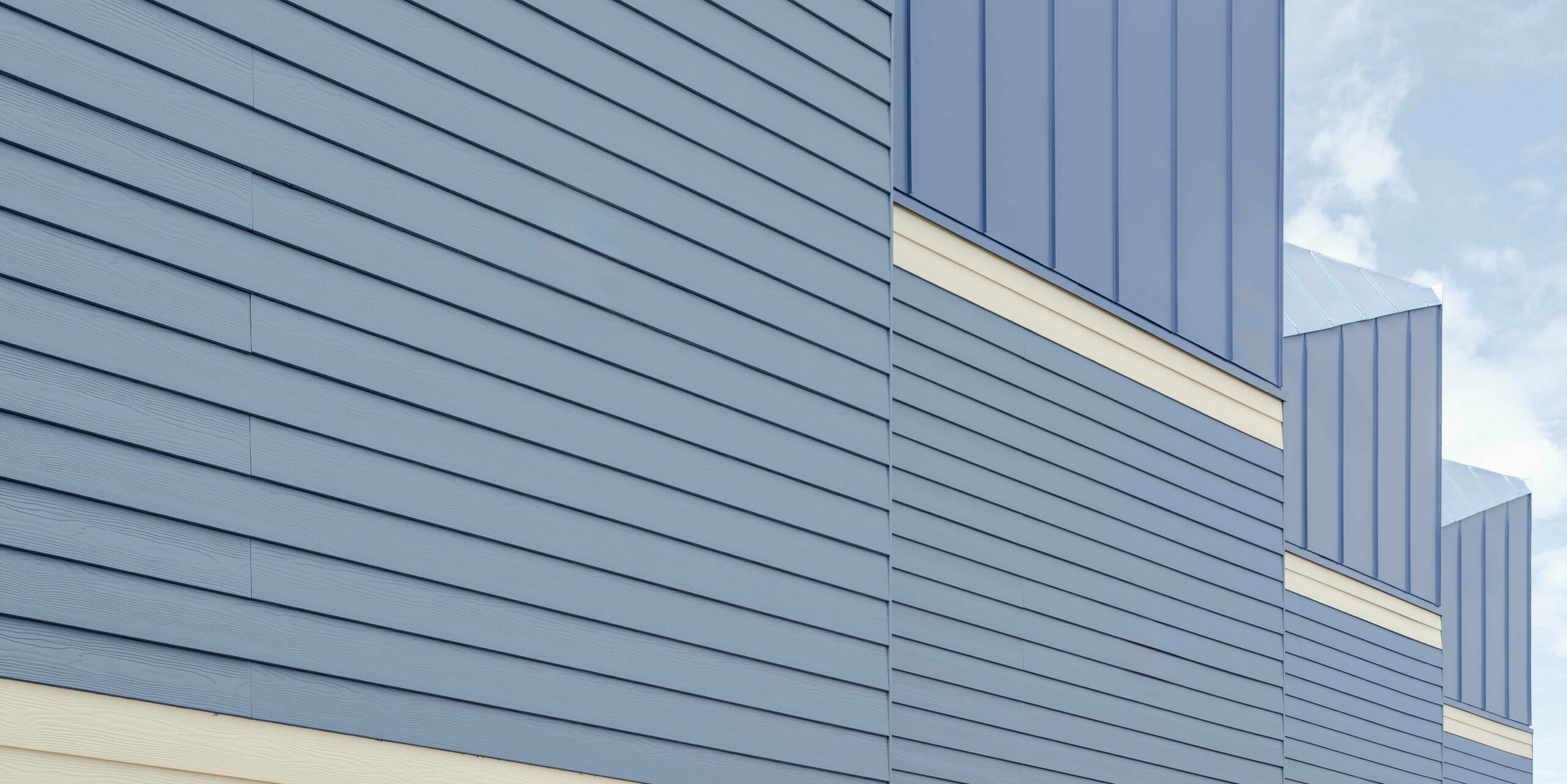 The photograph shows the striking façade of the Goldsmith Mews terraced houses with their eye-catching dusty blue PREFA FALZONAL standing seam aluminium cladding. The precise vertical lines of the aluminium surfaces create a lively structure and emphasise the modern architecture. The light-coloured basements lend the ensemble a sense of lightness and enhance the colour contrast. The durable, colour-stable PREFA aluminium provides long-term protection against the weather and enables a clear, long-lasting design that gives the project its distinctive character.