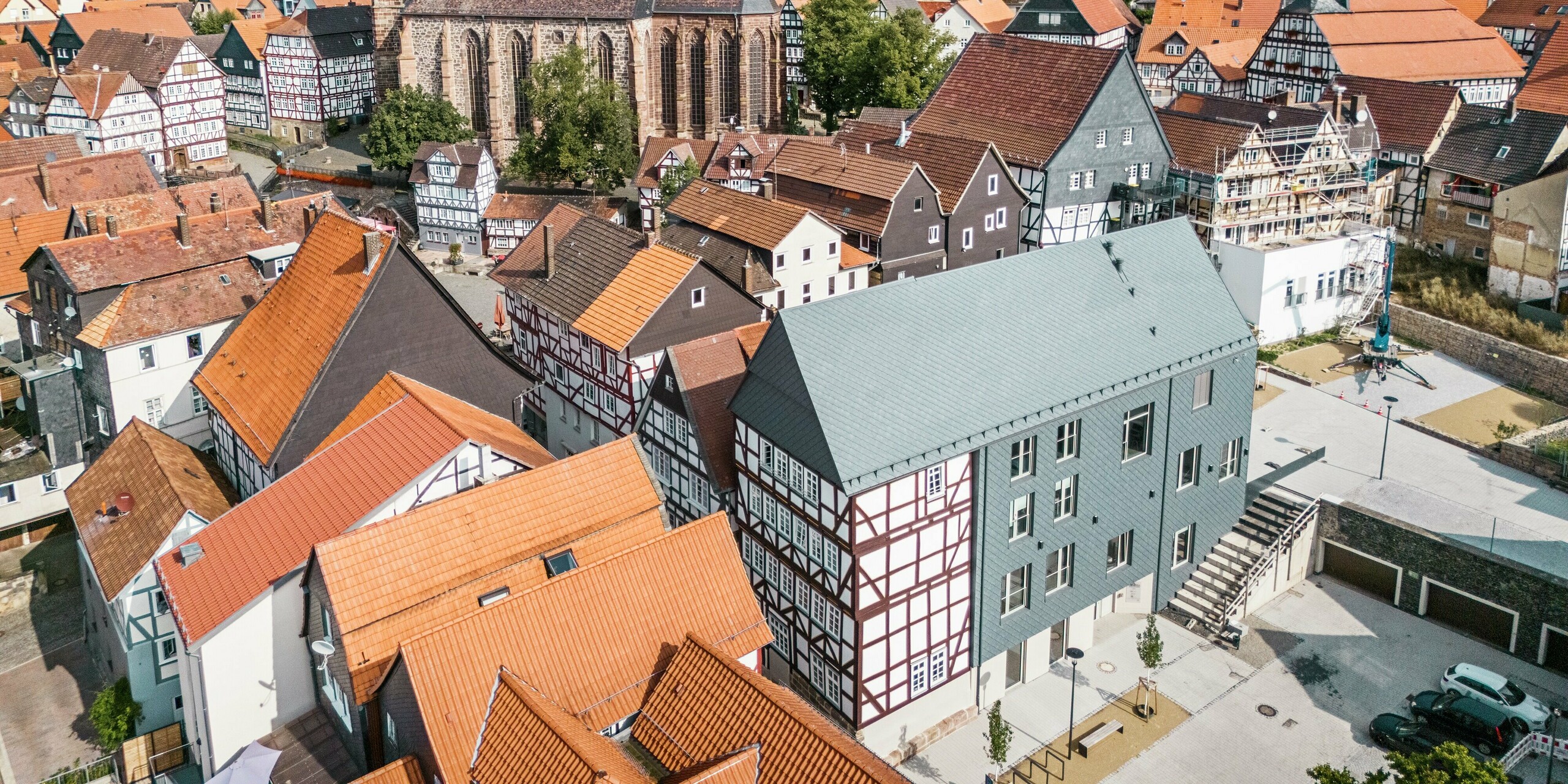 Weitwinkel-Drohnenaufnahme des Volkshauses in Homberg, DE, mit PREFA Dach- und Wandrauten 29 × 29 in P.10 Steingrau. Das moderne Design harmoniert mit der historischen Altstadt, die von Fachwerkhäusern, Kirche und Burg geprägt ist. Die schuppenartige Aluminiumbekleidung sorgt für Langlebigkeit und Witterungsbeständigkeit.