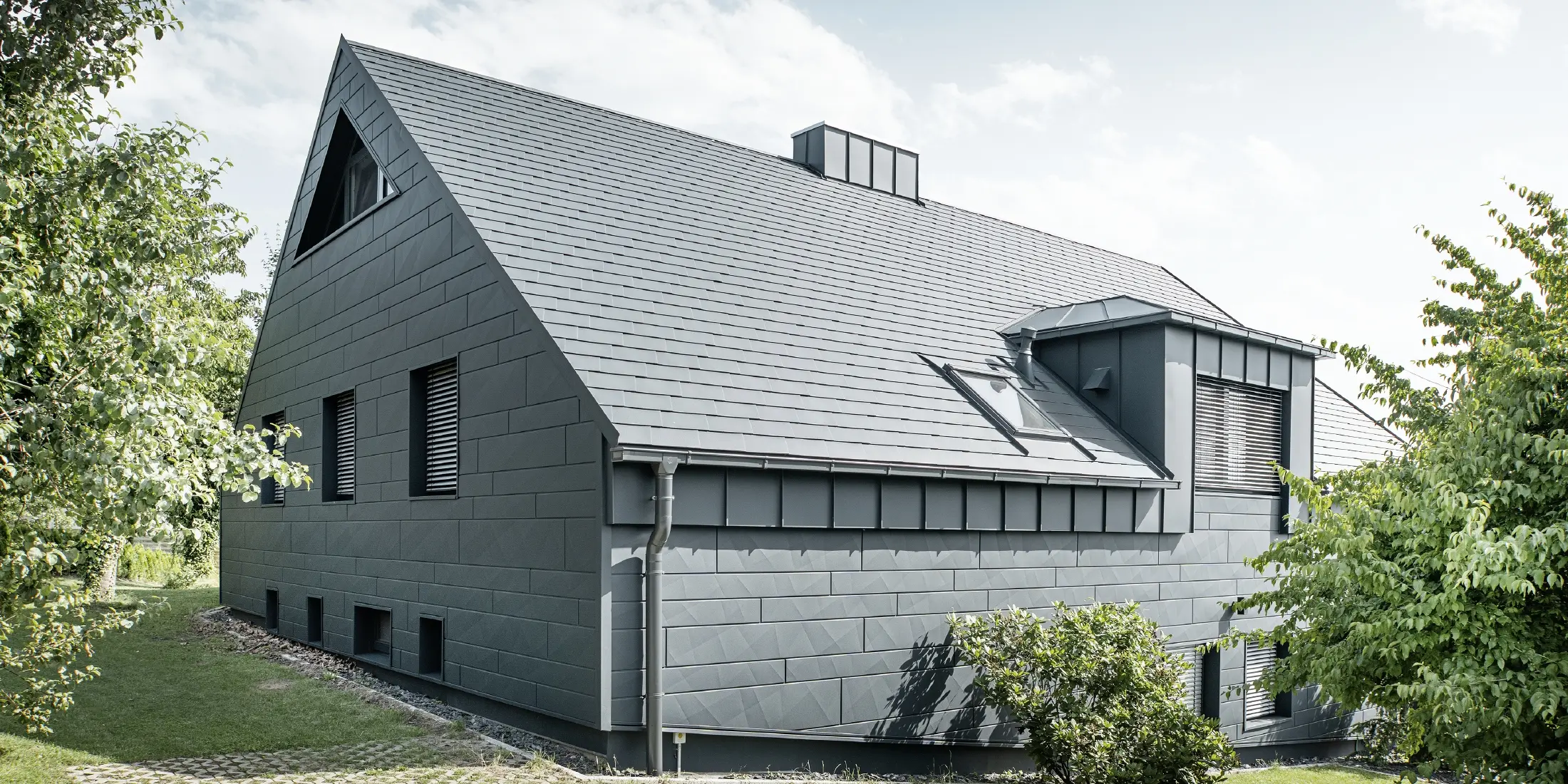 Large detached house with a gabled roof and lots of windows. The entire house was clad with an anthracite aluminium shell, PREFA aluminium shingles were used on the roof and Siding.X in anthracite on the façade.