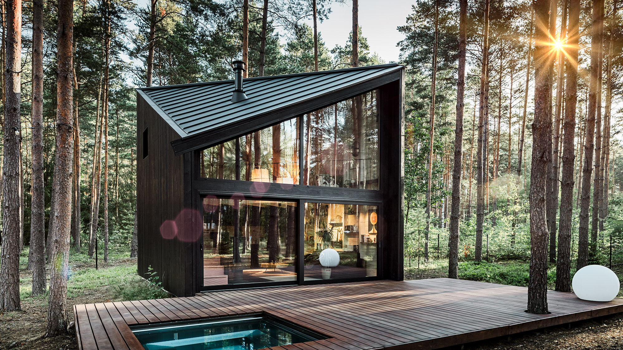 Side view of the holiday home with its diagonal Prefalz roof. The natural surroundings are reflected in the glazing.
