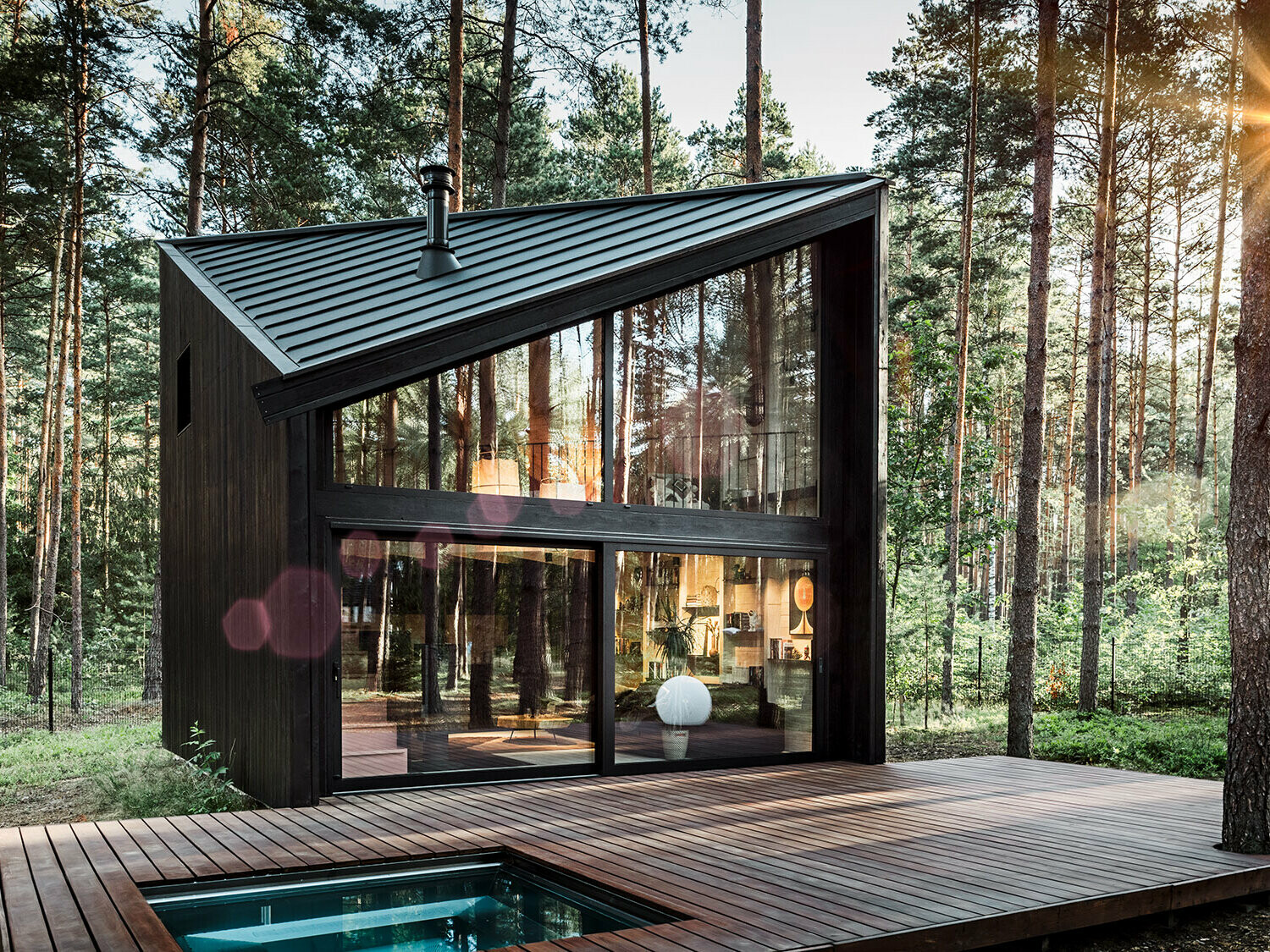 Side view of the holiday home with its diagonal Prefalz roof. The natural surroundings are reflected in the glazing.