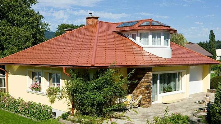 Detached house with a hipped roof and dormer clad with PREFA aluminium shingles in brick red to achieve a brick effect.