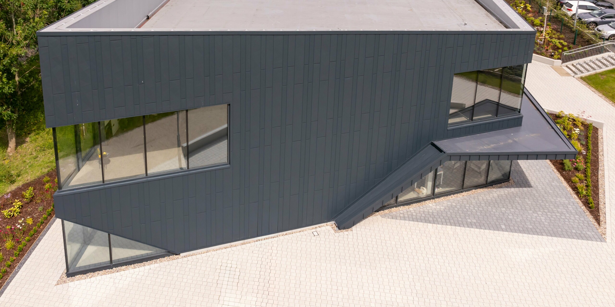 Bird's eye view of the front of the CREW building in Galway, Ireland, with modern PREFA façade made of Siding.X façade panels and PREFALZ in P.10 anthracite. The clear geometric shape of the building and the large window areas emphasise the innovative design. The anthracite-coloured aluminium cladding gives the building a timeless and professional appearance that blends harmoniously into the surrounding residential area.