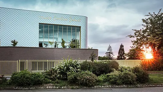 Das moderne Schulgebäude des Collège Léontine Dolivet in Cesson-Sévigné besticht durch seine markante Aluminiumfassade aus rund 15.000 PREFA-Wandelementen in Silbermetallic. Die glänzende Oberfläche reflektiert das Licht und verleiht dem Gebäude eine lebendige, elegante Ausstrahlung. Große Glasflächen eröffnen den Blick ins Grüne, während die robuste PREFA-Fassadenlösung Langlebigkeit und Witterungsbeständigkeit garantiert. Die Kombination aus wandelbarem Metall und klarer Architektur macht das Gebäude zu einem echten Blickfang und unterstreicht die Vorteile von Aluminium: geringes Gewicht, Wartungsfreiheit und Nachhaltigkeit.