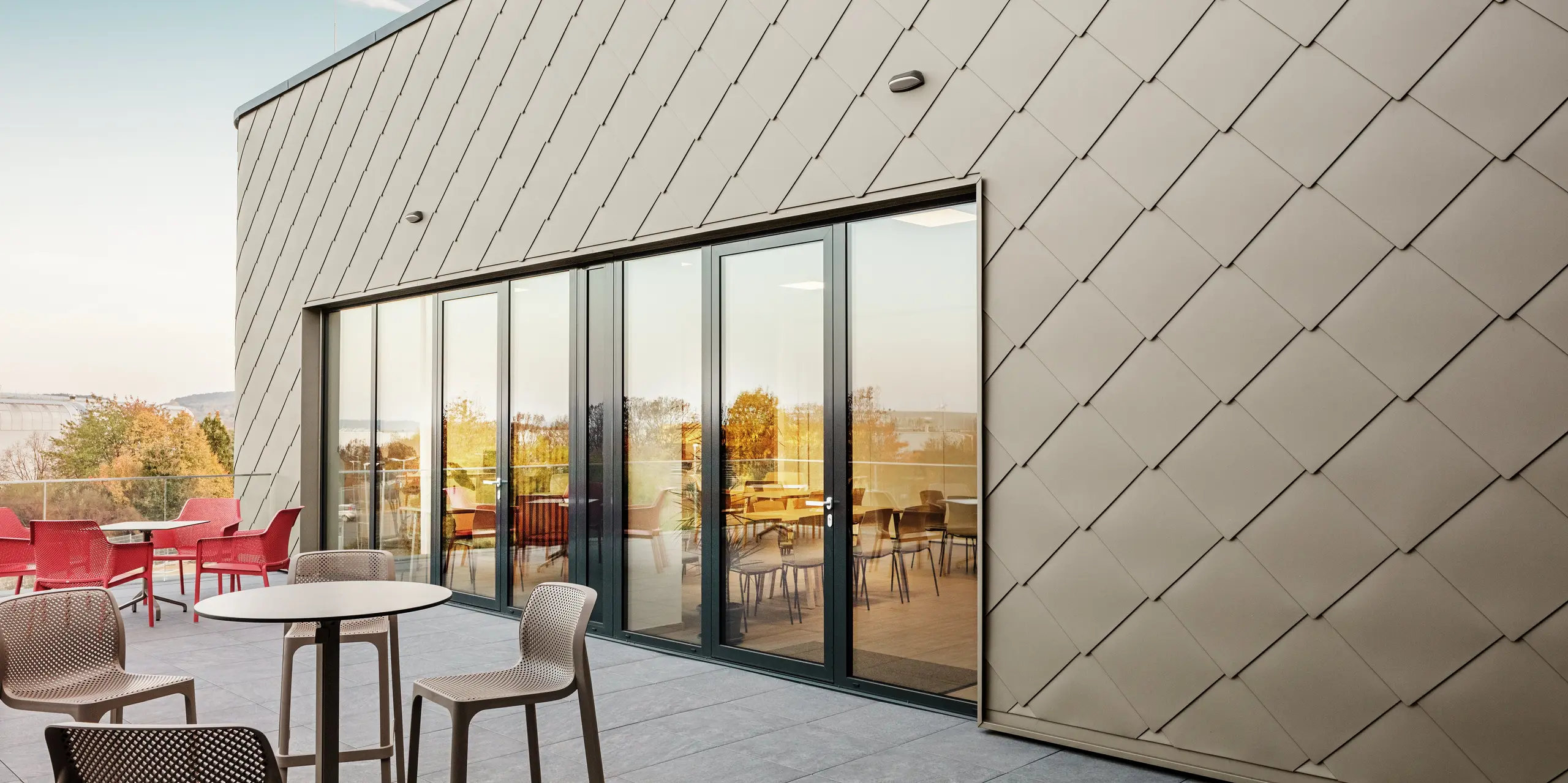 The façade of the new PREFA site in Törökbálint impresses with its elegant PREFA rhomboid façade tiles 44 × 44 in P.10 Prefabronze. The precisely installed aluminium façade ensures a modern, dynamic appearance while offering maximum protection against the elements. The generous glass front connects the internal and external areas and creates a bright and inviting atmosphere on the spacious terrace.