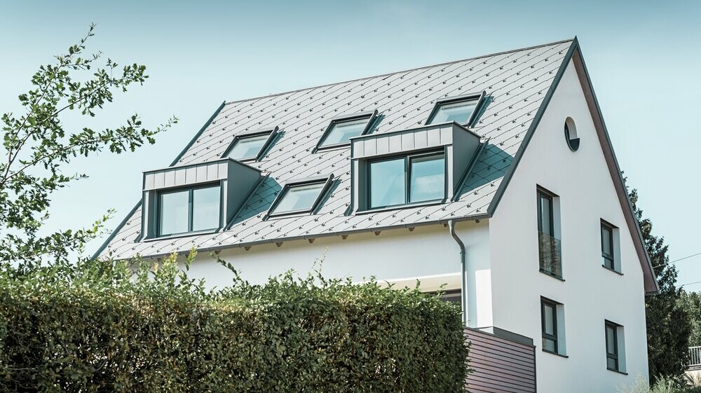 Roof refurbishment of a gabled roof with two dormers and four roof windows. The roof was covered with PREFA light grey 44 × 44 rhomboid roof tiles. The PREFA hanging gutter, also in light grey, was used for the guttering. 