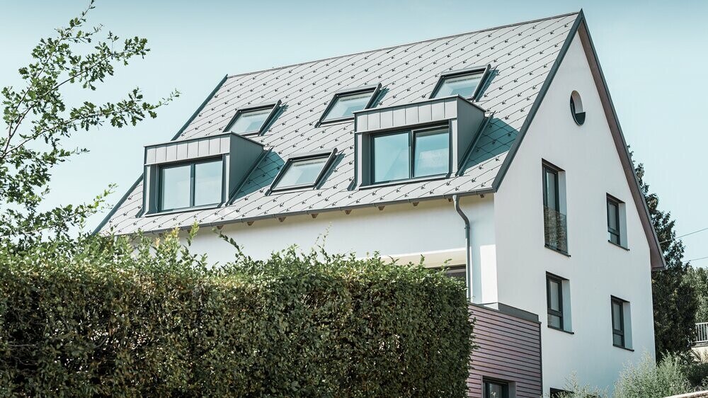 Roof refurbishment of a gabled roof with two dormers and four roof windows. The roof was covered with PREFA light grey 44 × 44 rhomboid roof tiles. The PREFA hanging gutter, also in light grey, was used for the guttering. 