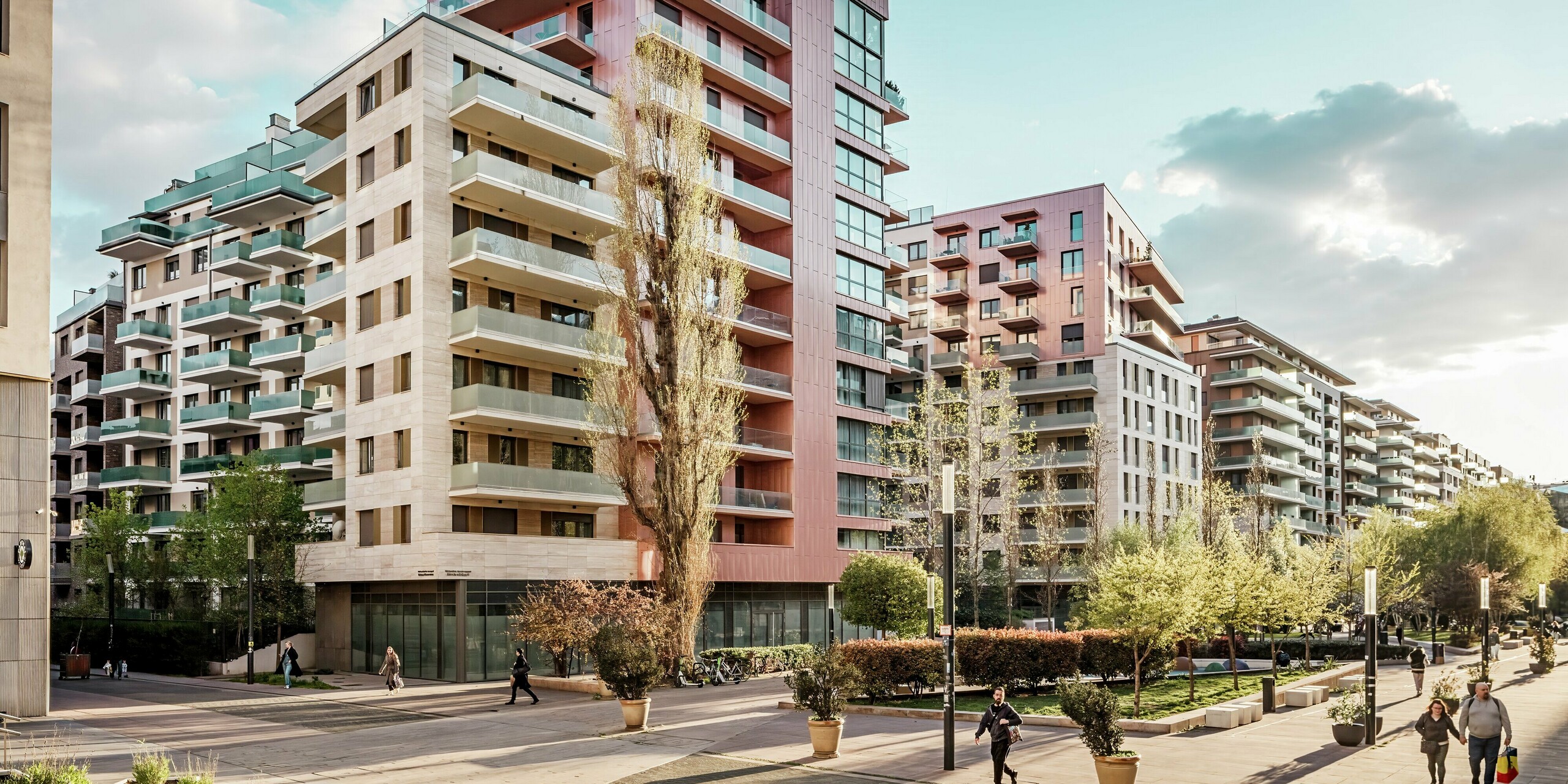 Straßenszene entlang der Corvin-Promenade in Budapest mit dem prägnanten Wohnensemble Grand Corvin im Vordergrund. Die oberen Etagen sind mit vertikal verlegten PREFA Sidings in der Sonderfarbe Lachsmetallic verkleidet und setzen moderne Akzente im urbanen Raum. Die langlebige Aluminiumverkleidung verbindet Design, Qualität und Witterungsbeständigkeit in einem der größten Stadterneuerungsprojekte Mitteleuropas.