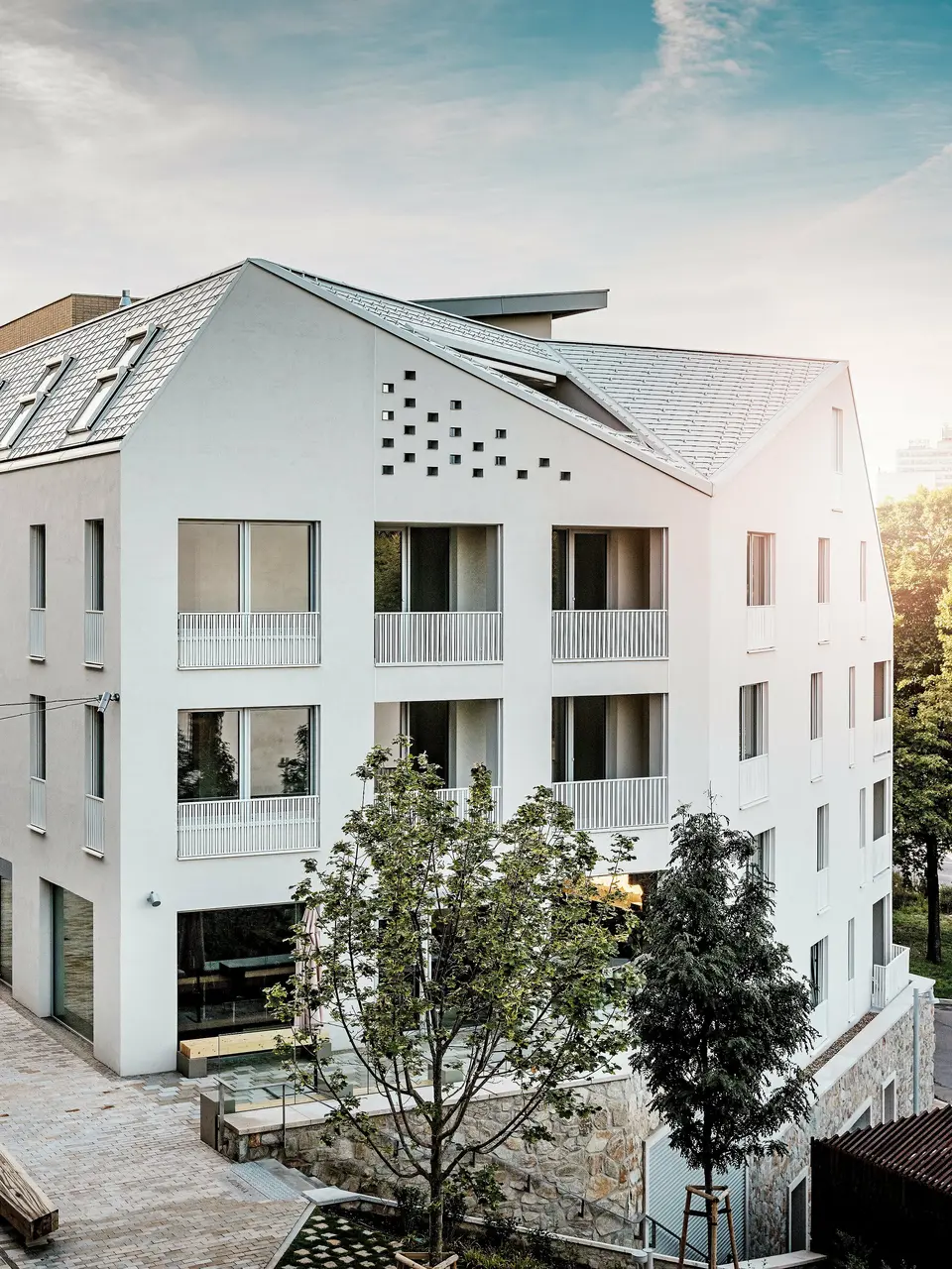 Modernes Wohnquartier Vydrica in Bratislava mit klarer Architektursprache und ruhiger Gassenatmosphäre: Die steil geneigten Satteldächer mit markanten Dachfenstern sind mit PREFA Aluminium Dachschindeln in P.10 Prefaweiß, Bronze und P.10 Sandbraun gedeckt und bilden einen eleganten Eyecatcher im Sonnenlicht. Die präzise ausgeführten Linien und homogenen Flächen unterstreichen die hochwertige Gestaltung. PREFA Aluminium überzeugt durch Langlebigkeit, geringes Gewicht und hohe Witterungsbeständigkeit – ideal für komplexe Dachformen und eine nachhaltige, wartungsarme Gebäudehülle.