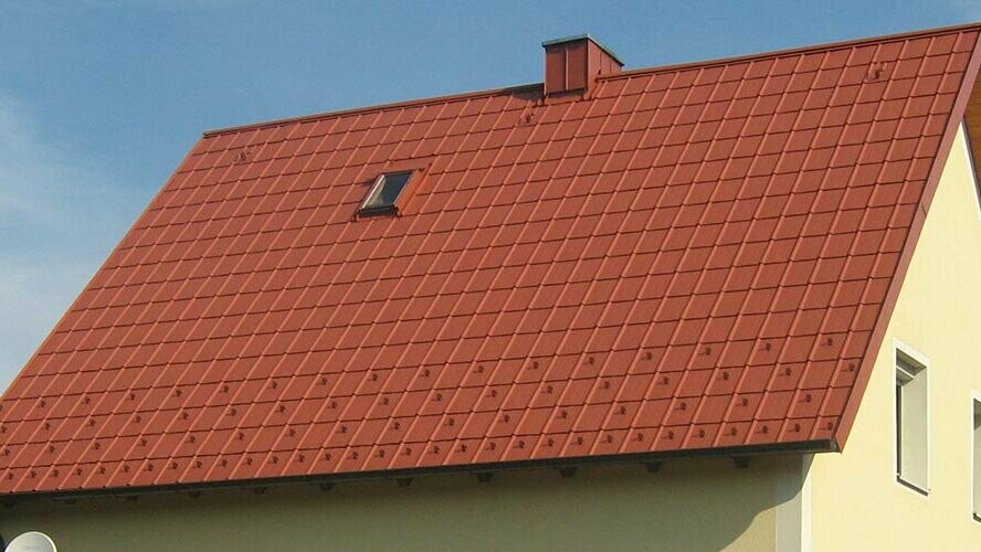 Traditional gable roof with small skylight and chimney, covered with PREFA roof tiles in brick red, including snow guards and roof safety hooks.