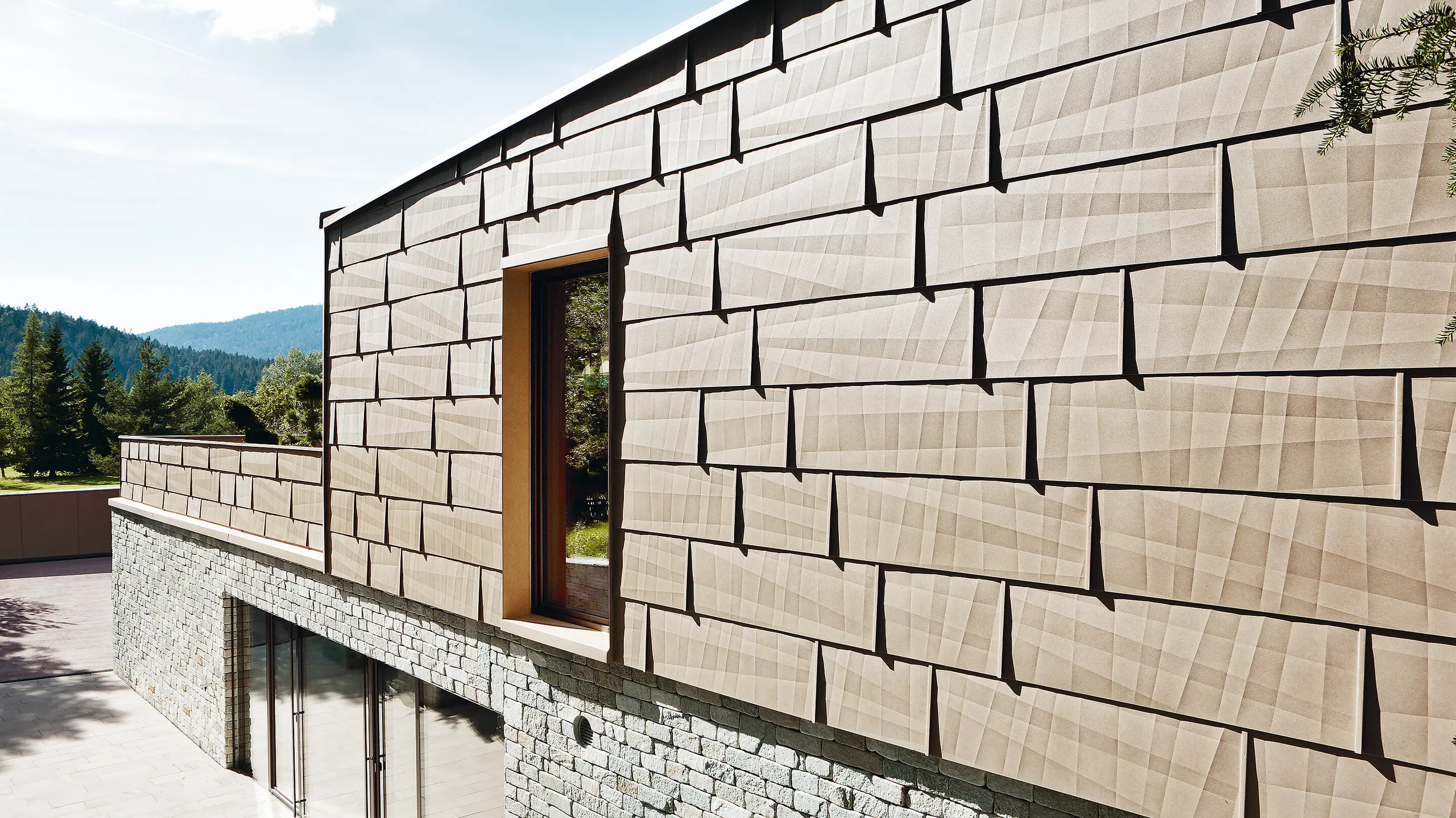 On this external façade, the PREFA FX.12 façade panel in P.10 sand brown has been combined with a stone façade on the bottom floor.