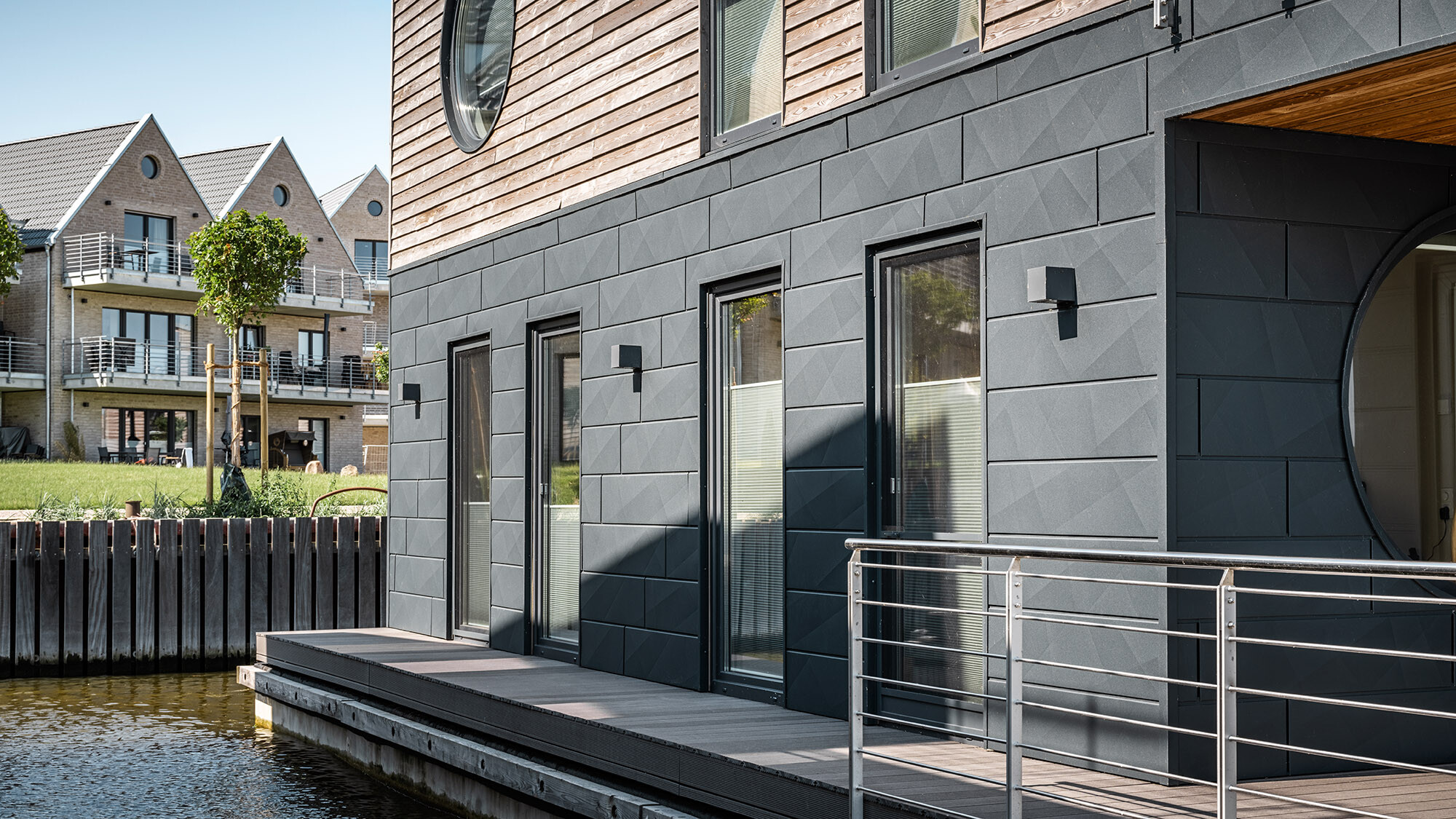 The siding.X façade from up close; the Schlei extends right before it, and in the back, to the side, residential buildings can be seen on the mainland.