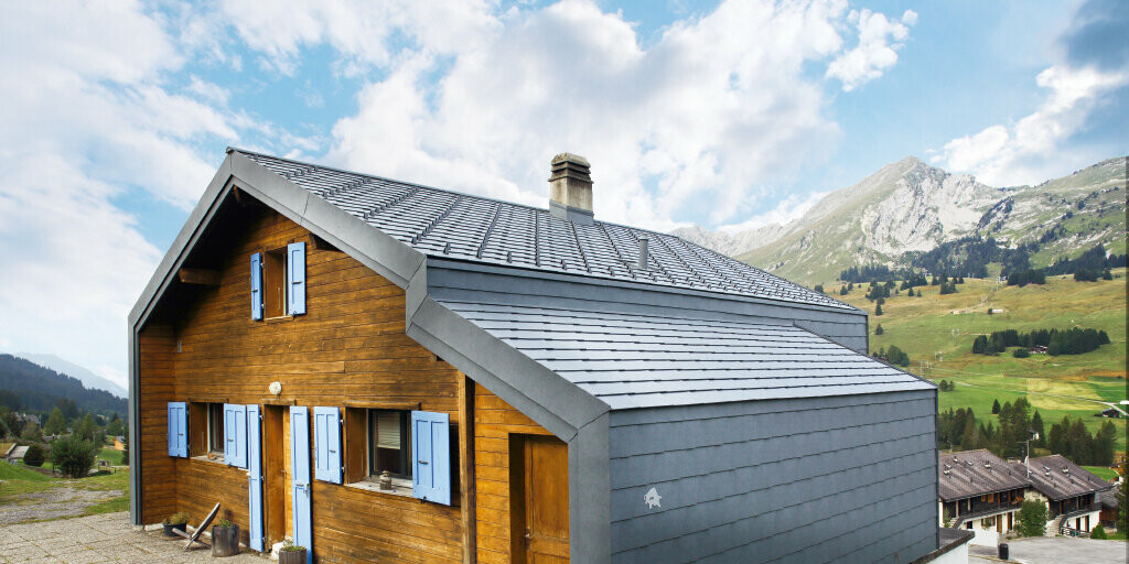 House in the Swiss mountains with a wooden façade combined with the PREFA rhomboid roof and façade tiles in stone grey