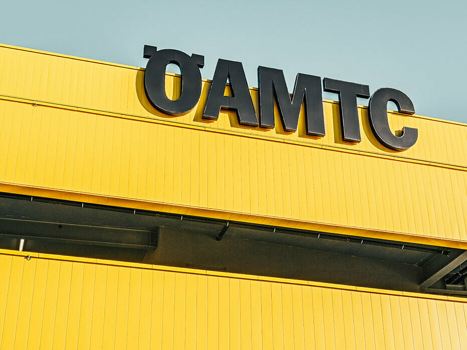 Close-up of the ÖAMTC Logo. The façade is covered in PREFA Sidinds in the bespoke colour rapeseed yellow and slate grey.