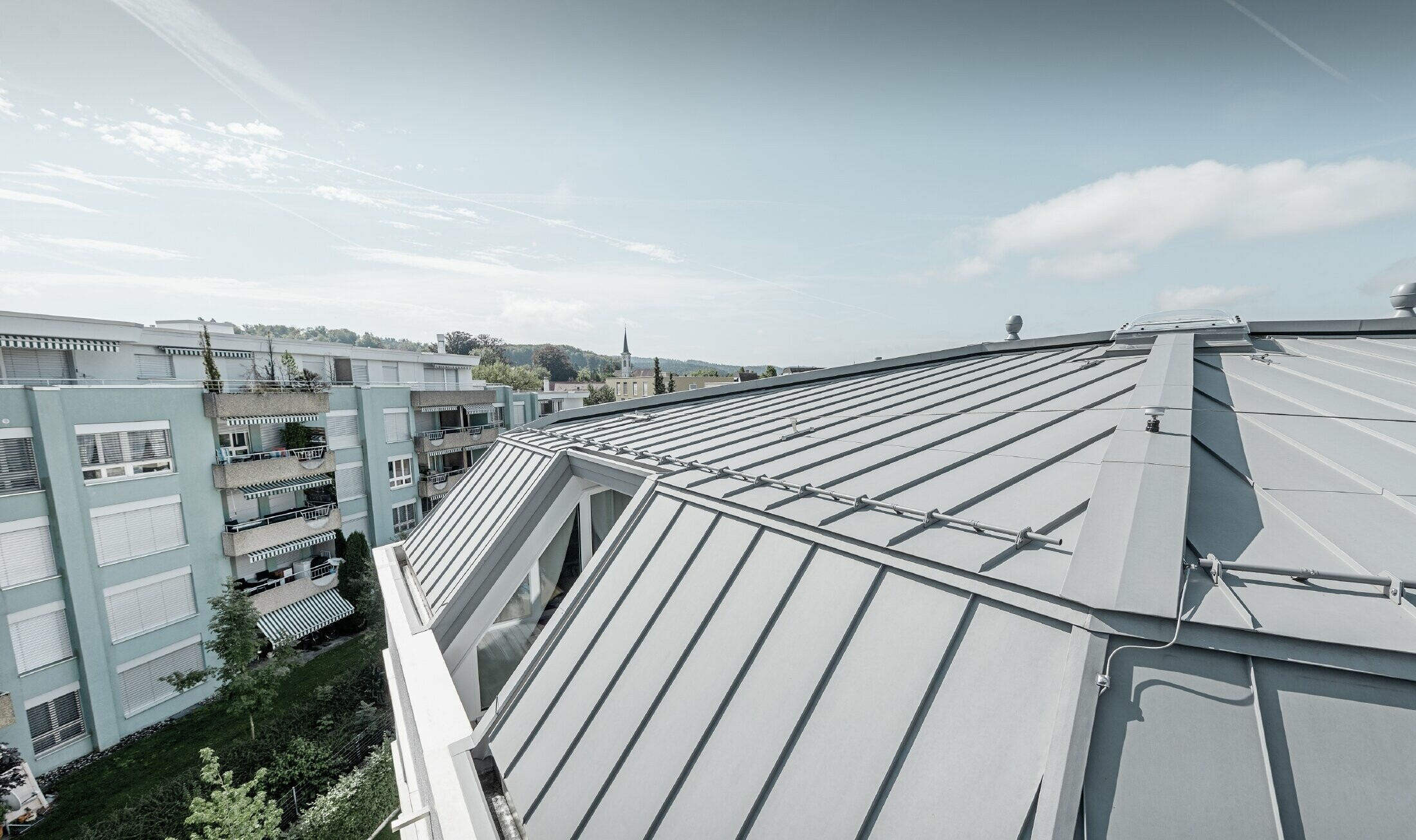 Close up of the roof area of an apartment building. Standing seam roof designed with PREFA Prefalz in patina grey.